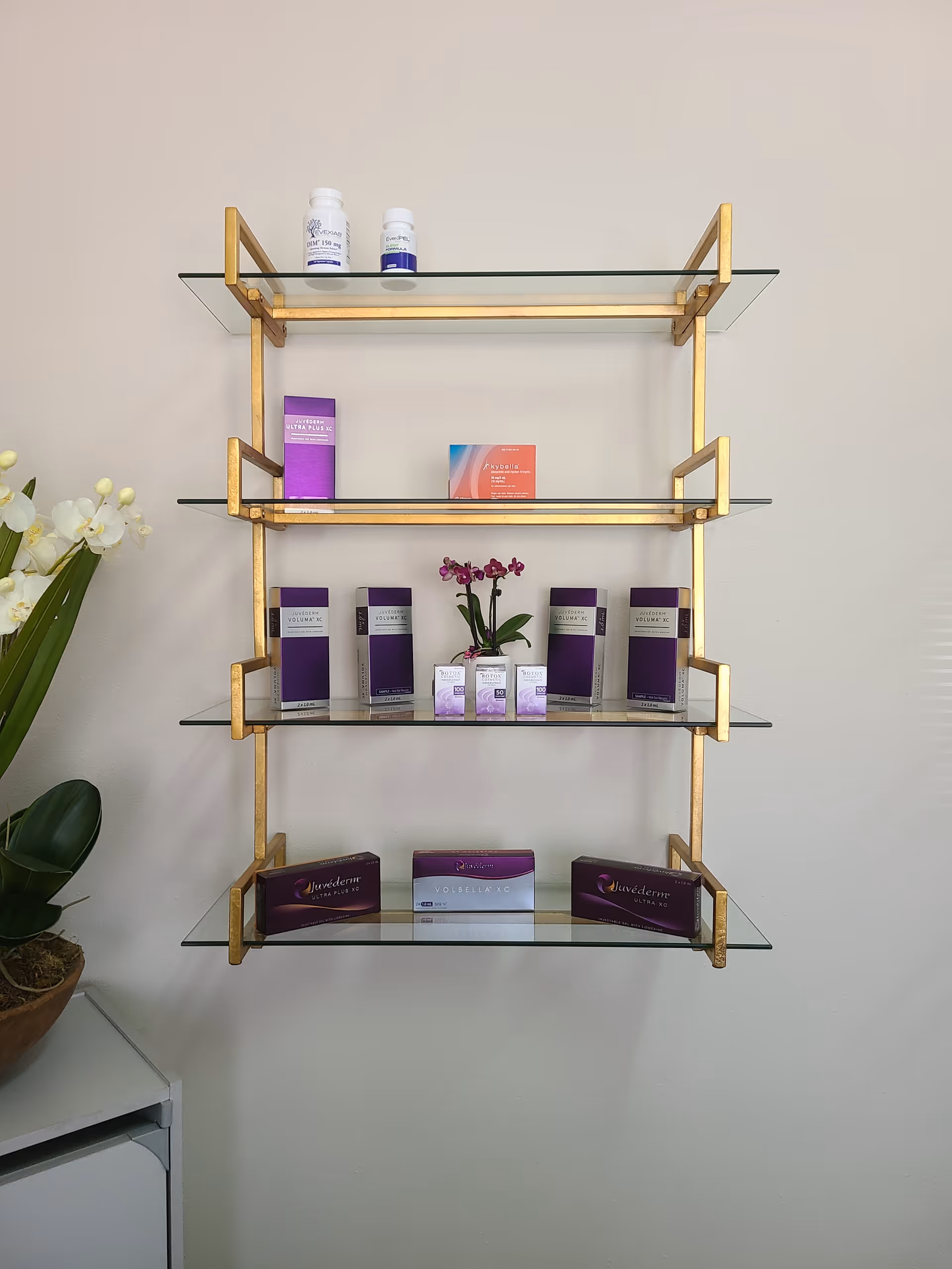 Gold-framed glass shelves holding skincare products on a cream wall.