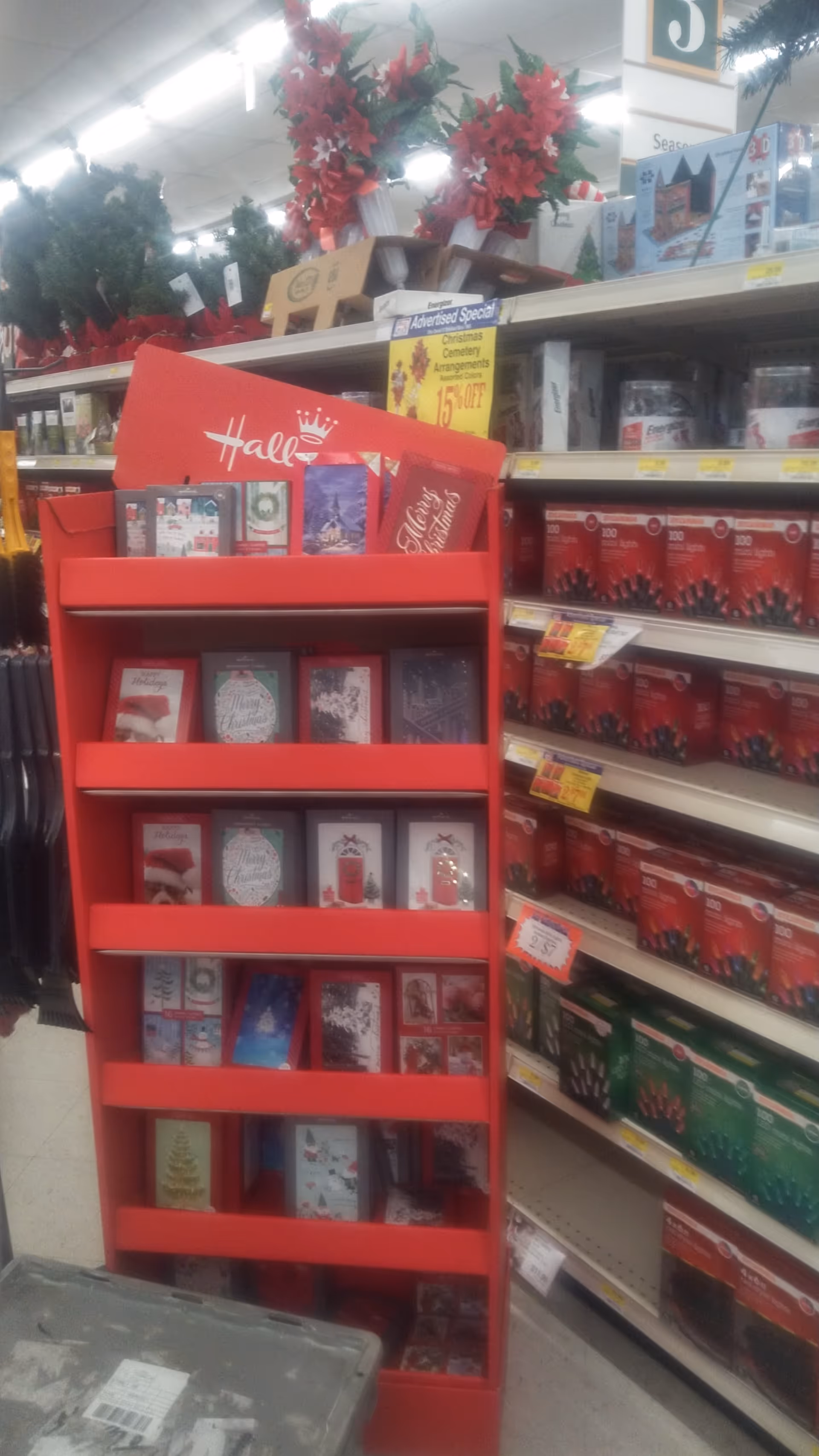 Red holiday card display stands in aisle, surrounded by shelves of merchandise inside Discount Drug Mart.