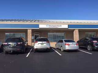 Front exterior of a brick health facility with a blue accent and parked cars.