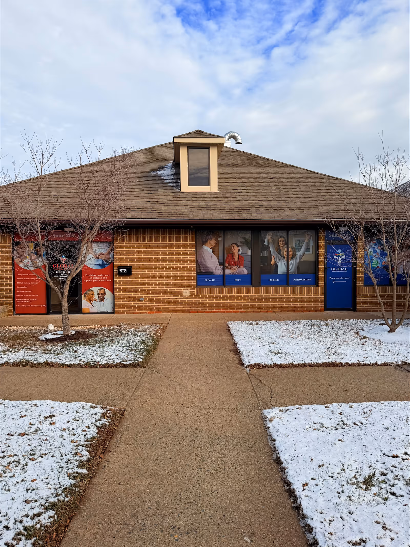 Exterior view of a brick senior living facility with a snowy landscape and walkway.