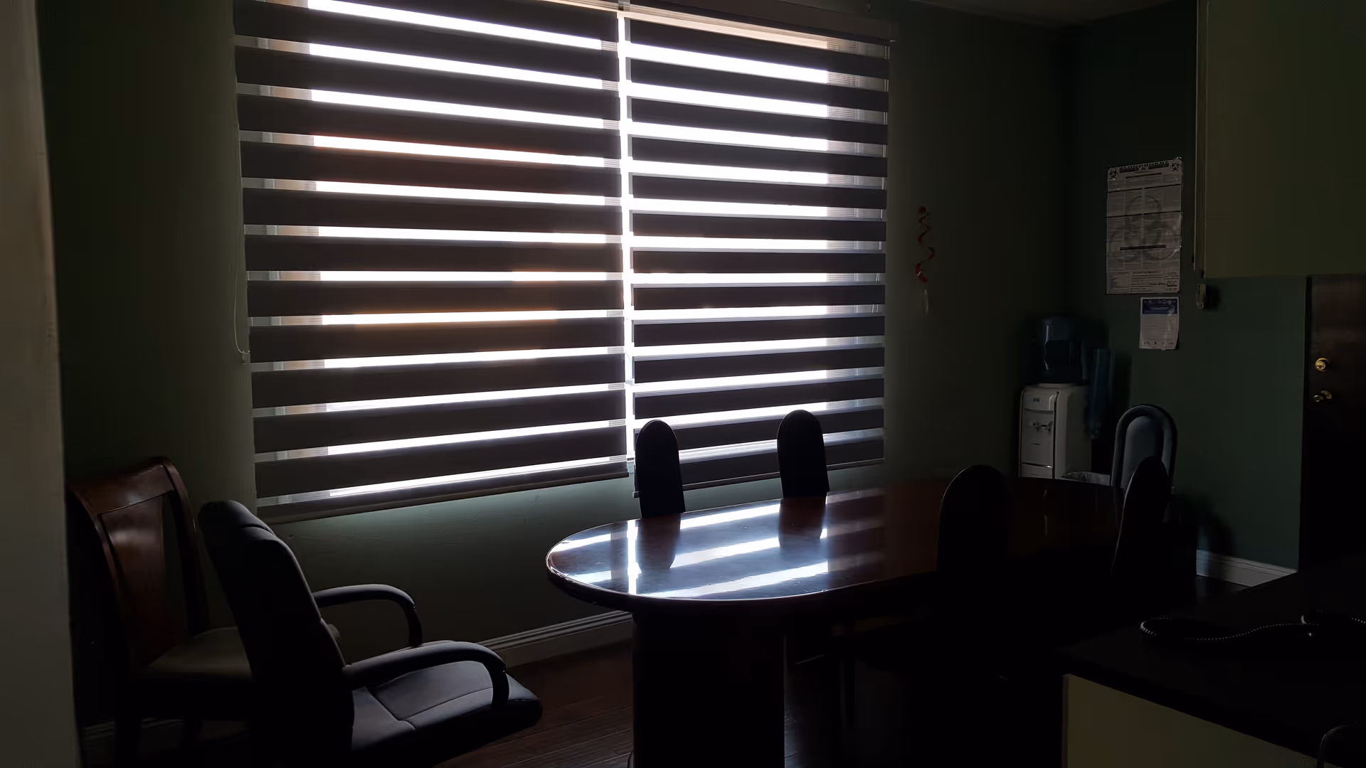 Dimly lit dining area with a wooden oval table and striped blinds.