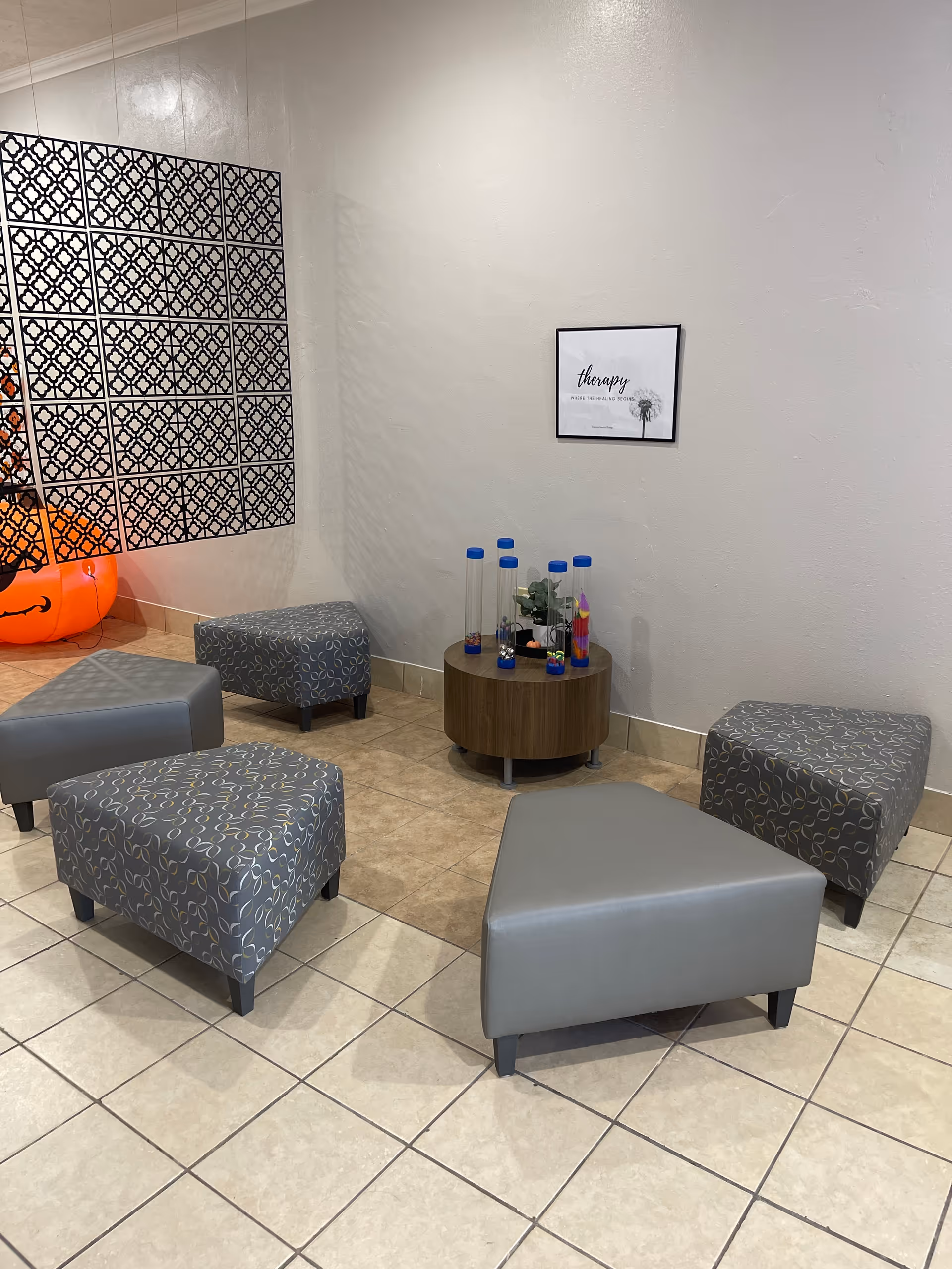 Gray tiled lobby seating area with patterned ottomans, a small round table, and water bottles.