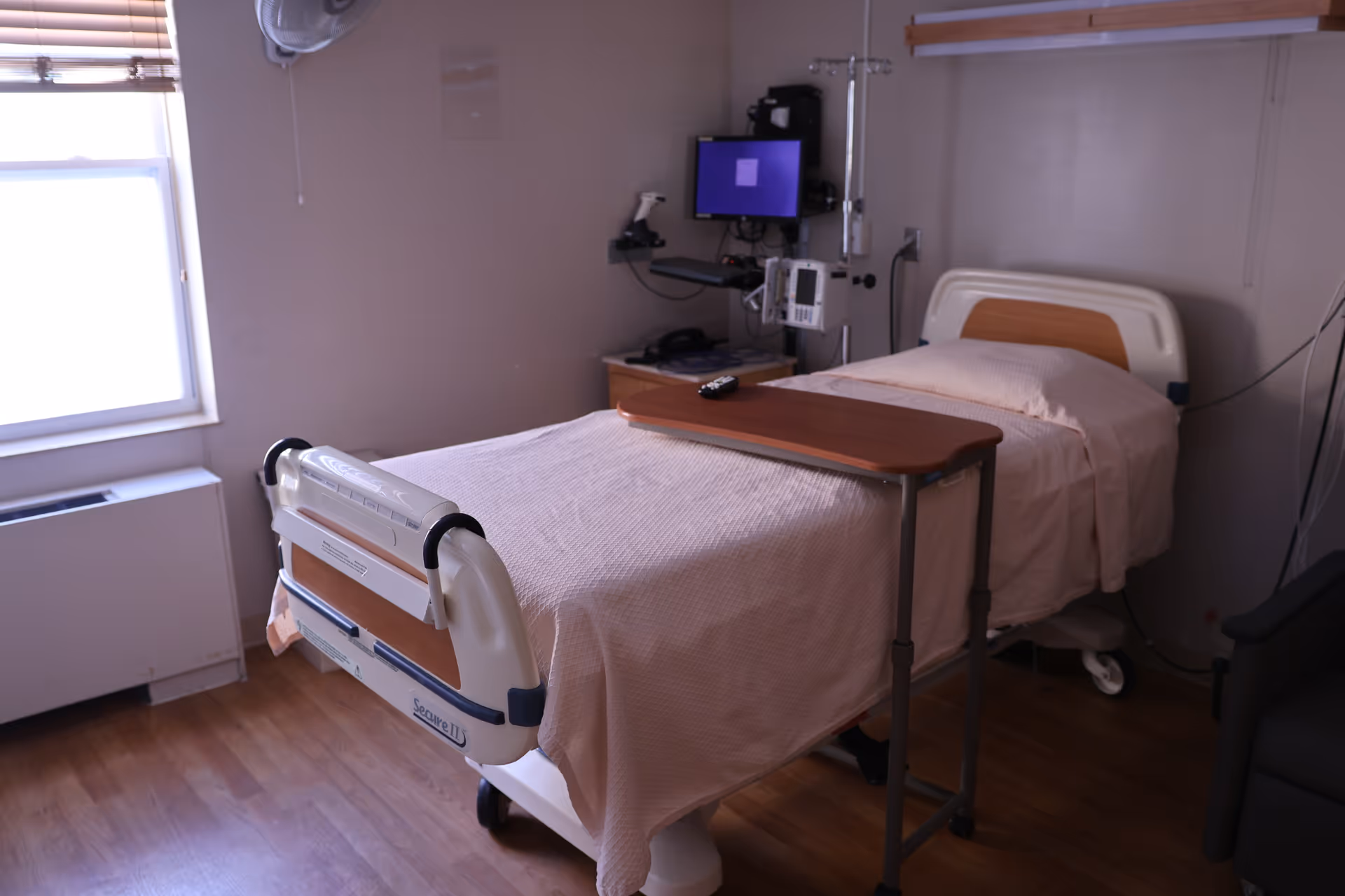 Hospital-style patient bed in a small room with medical equipment and a window.