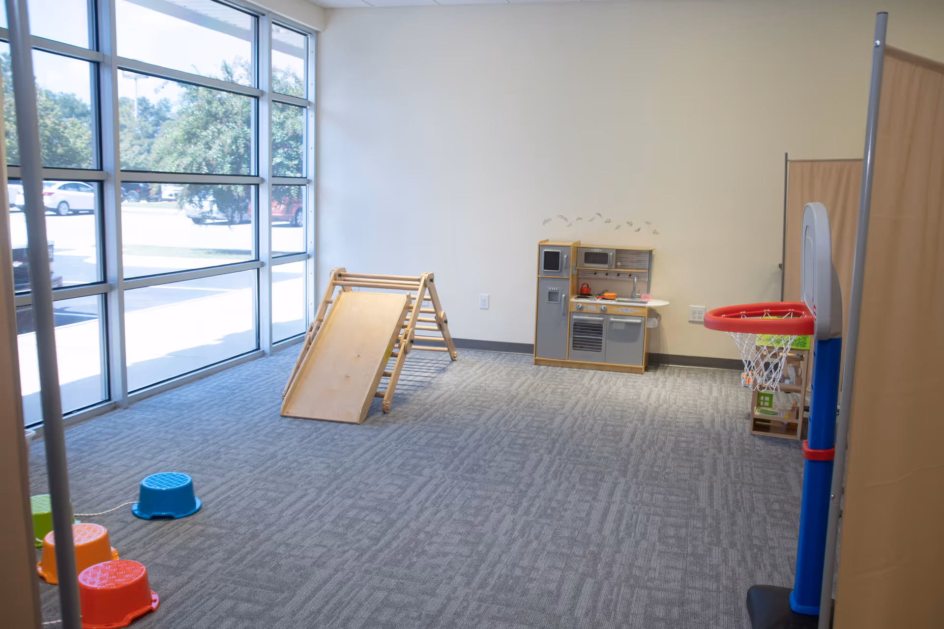 Bright play area with a wooden ramp slide, toy kitchen, mini basketball hoop, and seating.