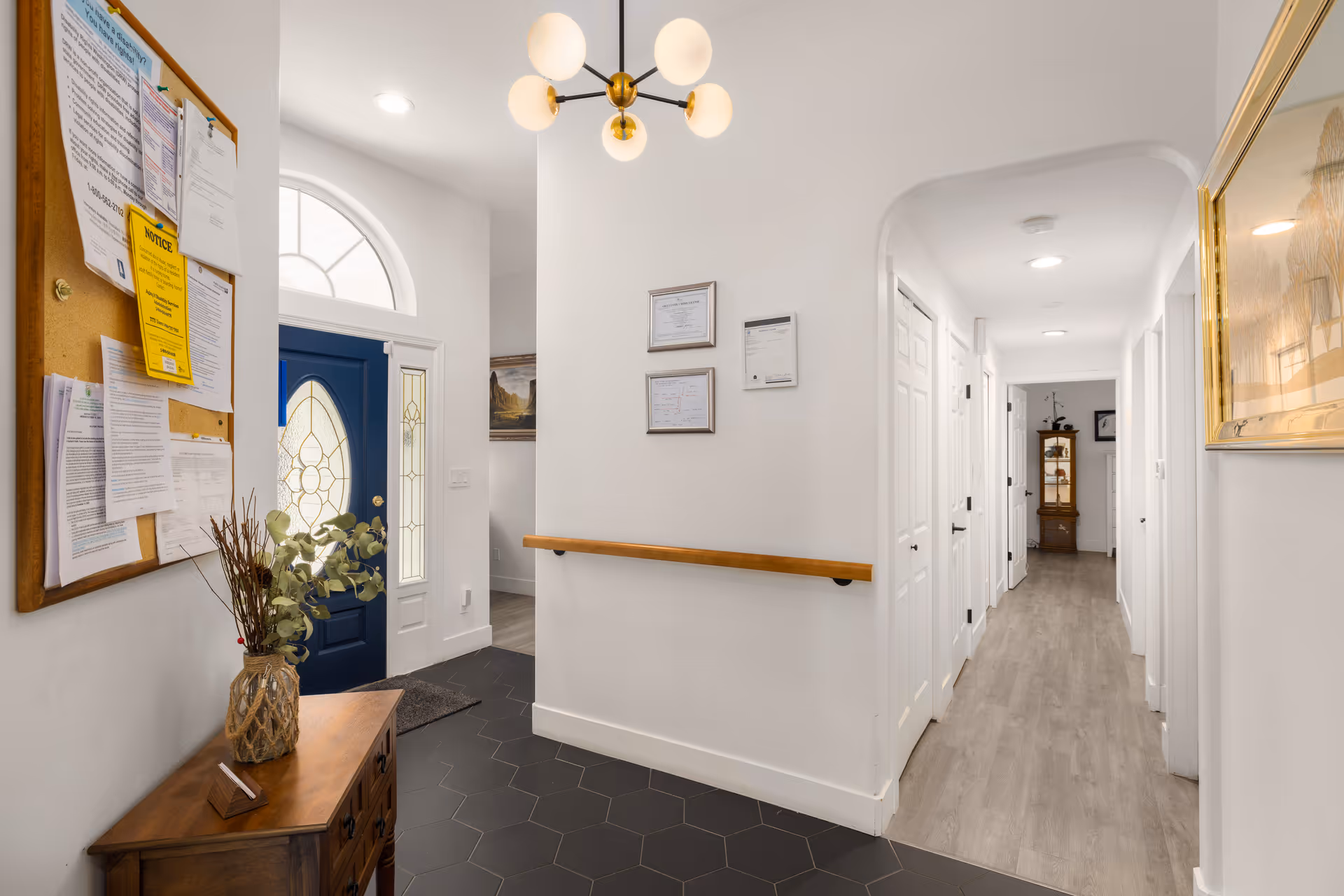 Bright hallway interior with a blue front door, bulletin board, and framed certificates along white walls.