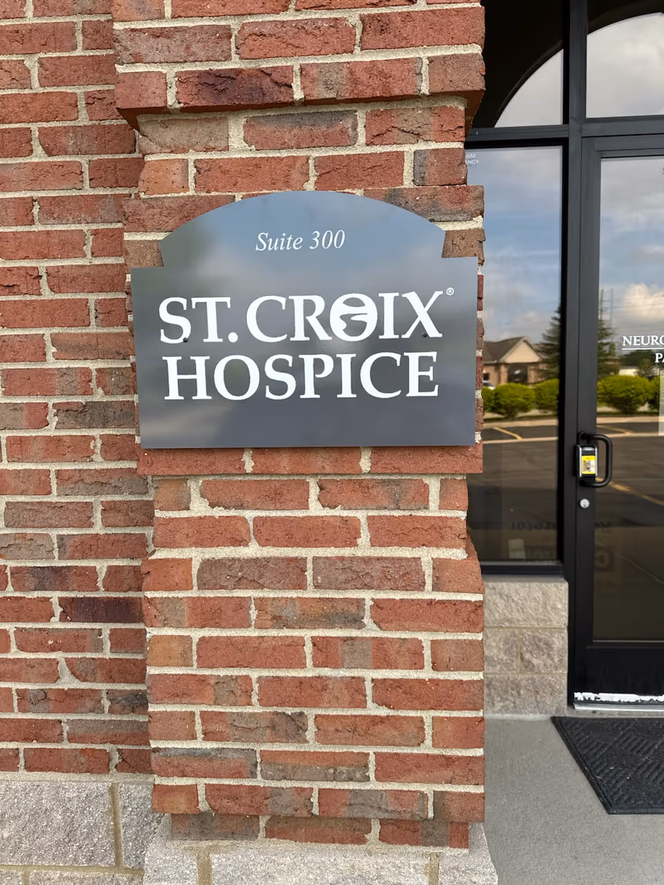 Brick exterior with St. Croix Hospice Suite 300 sign beside glass entrance door