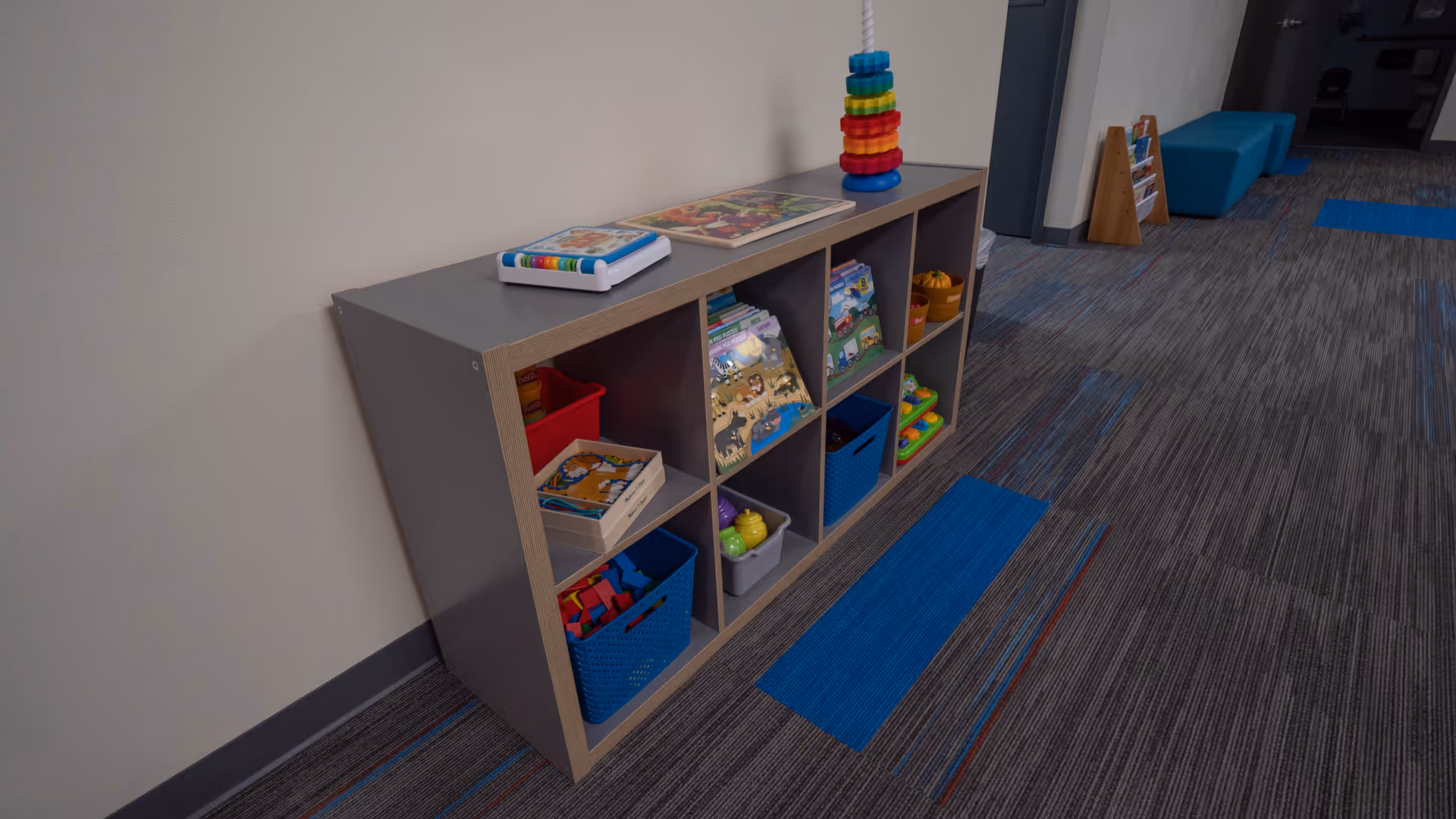 Hallway with cubby storage of toys and books along a wall in a play area.
