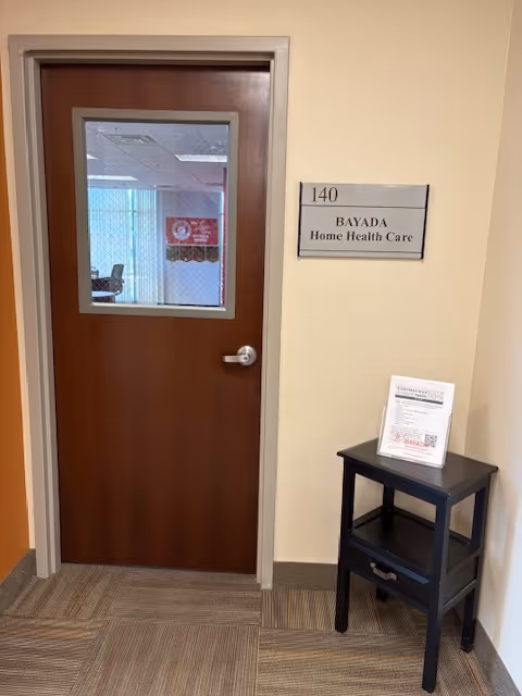 Wooden door with BAYADA sign in a hallway beside a small black table.