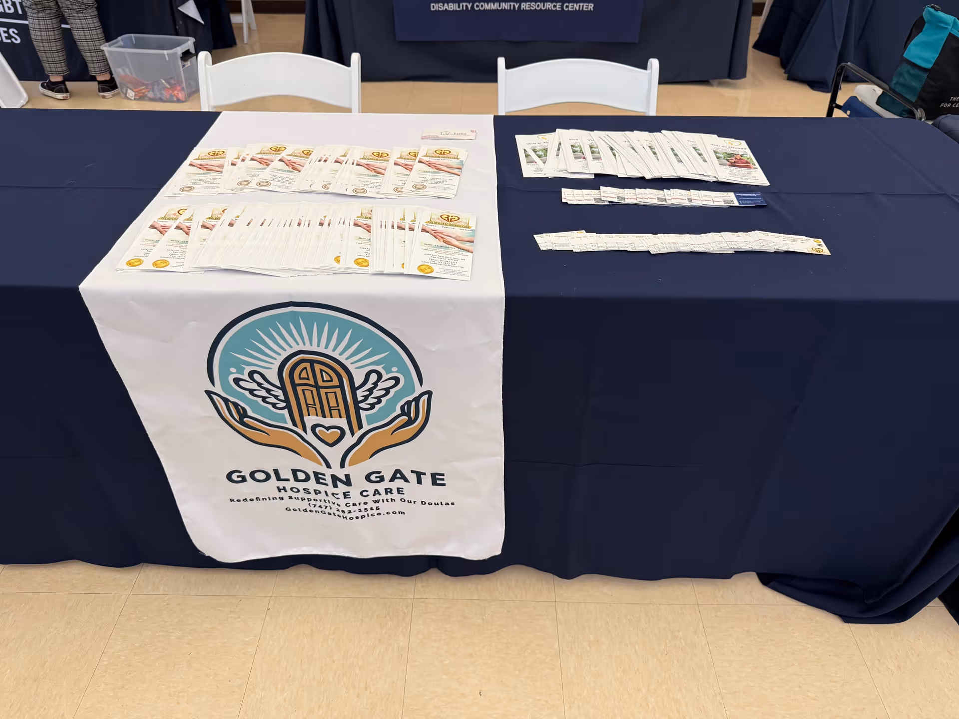 A table is draped in navy cloth with a Golden Gate Hospice Care banner and brochures.