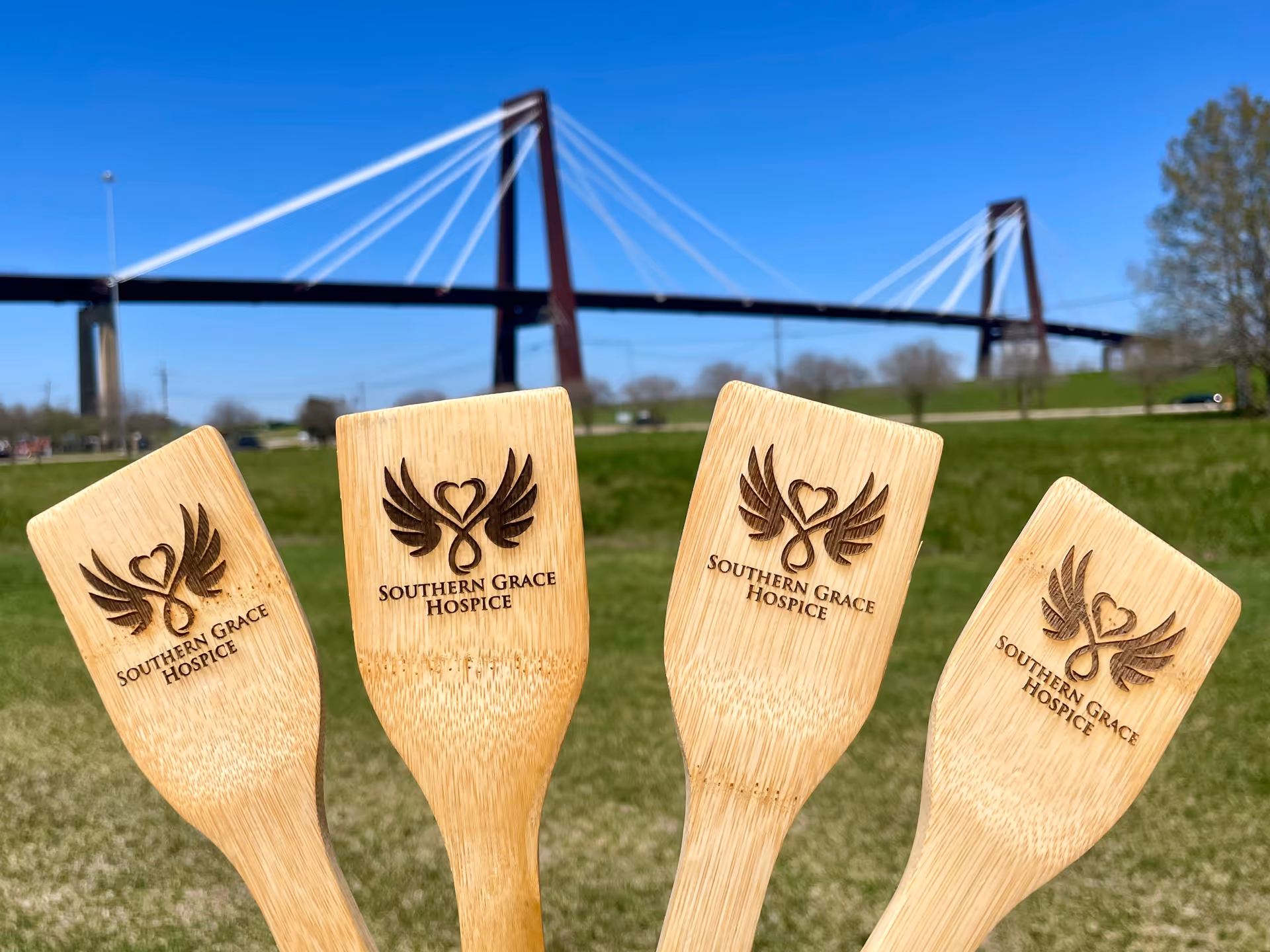 Four wooden paddles with Southern Grace Hospice logos in a grassy field and a bridge.
