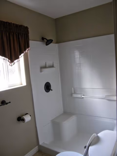 White tiled bathroom with a shower, grab bars, and toilet.
