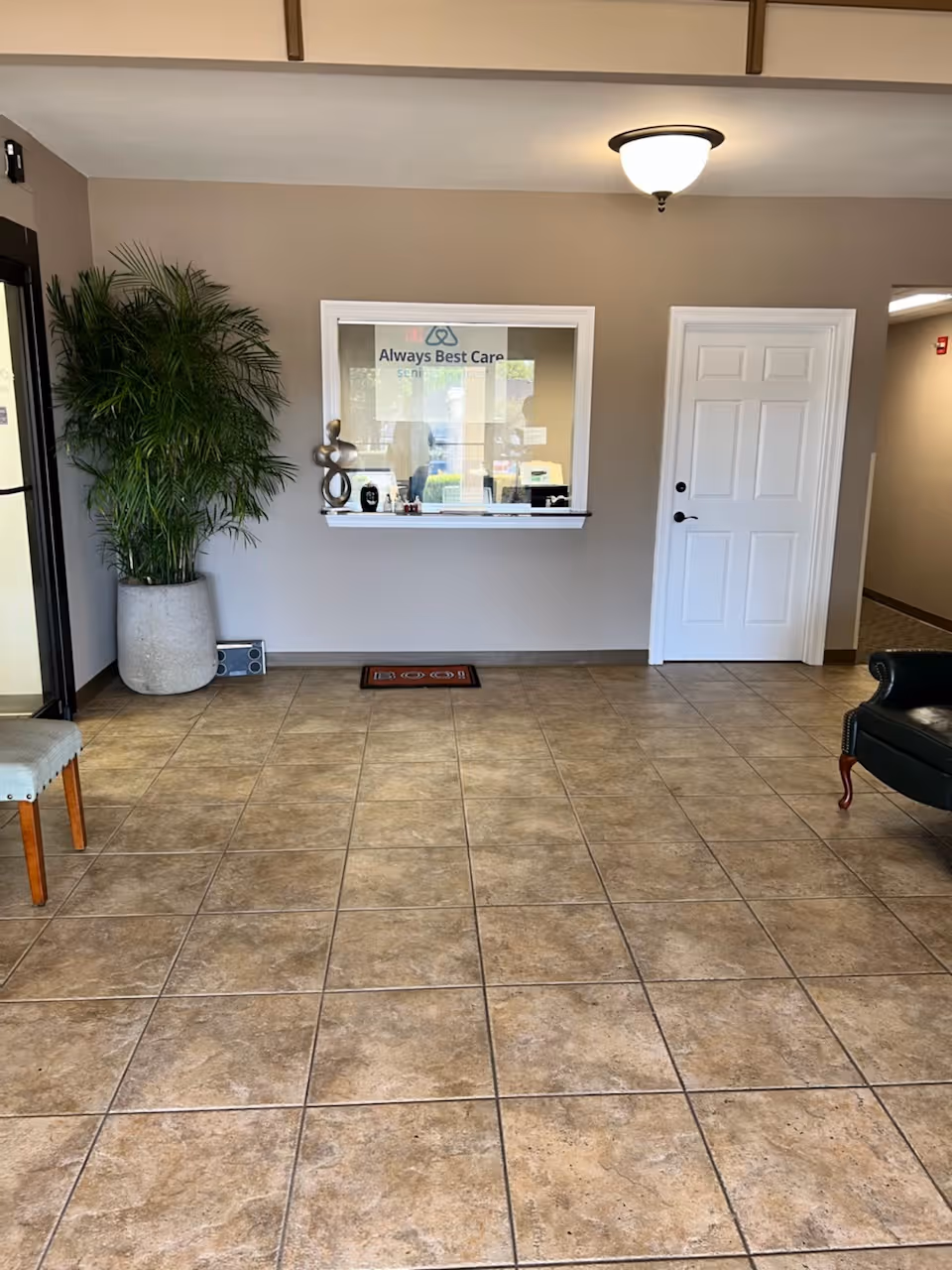 Lobby reception window of a senior services facility, with plant, seating, and beige walls.