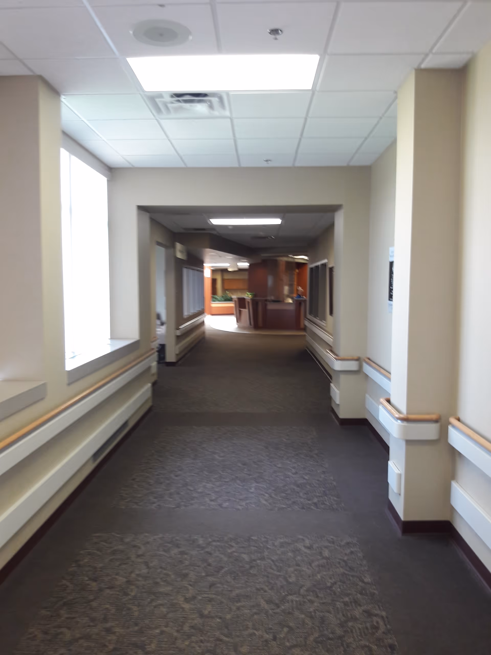 Long interior hallway of a senior living center, carpeted floor, leading to a seating area.