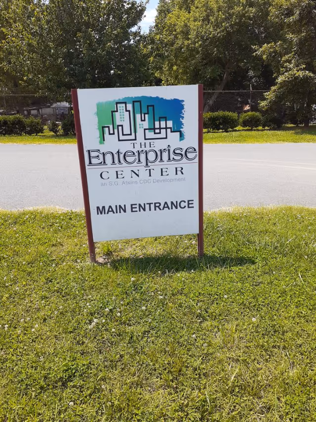 Outdoor scene with a white sign reading The Enterprise Center Main Entrance on a grassy lot