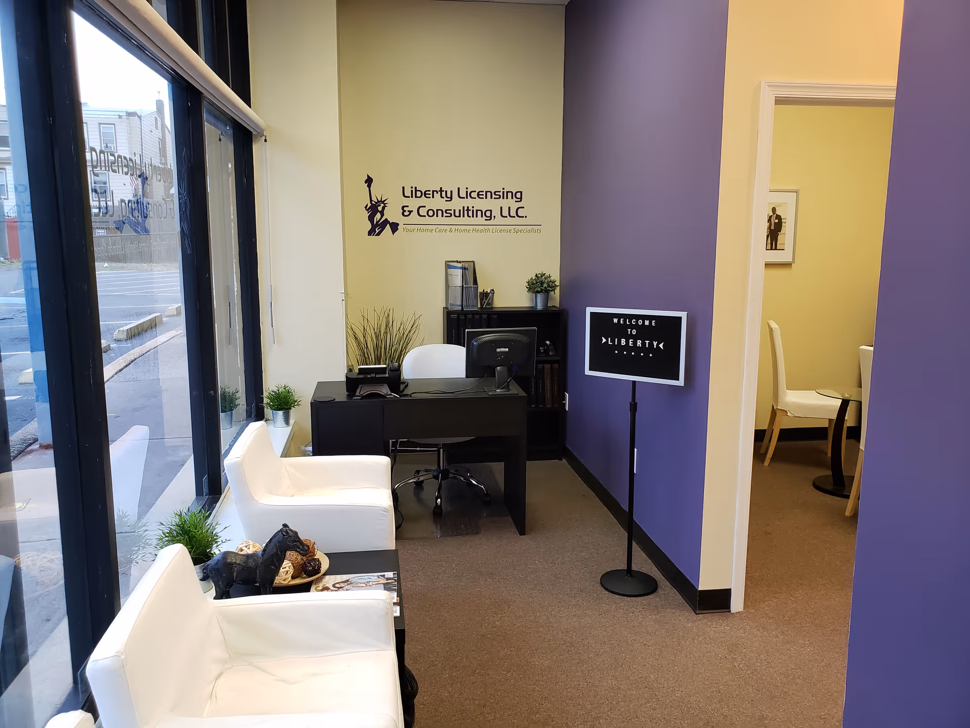Reception area with a desk, white chairs, plants, and a welcome sign.
