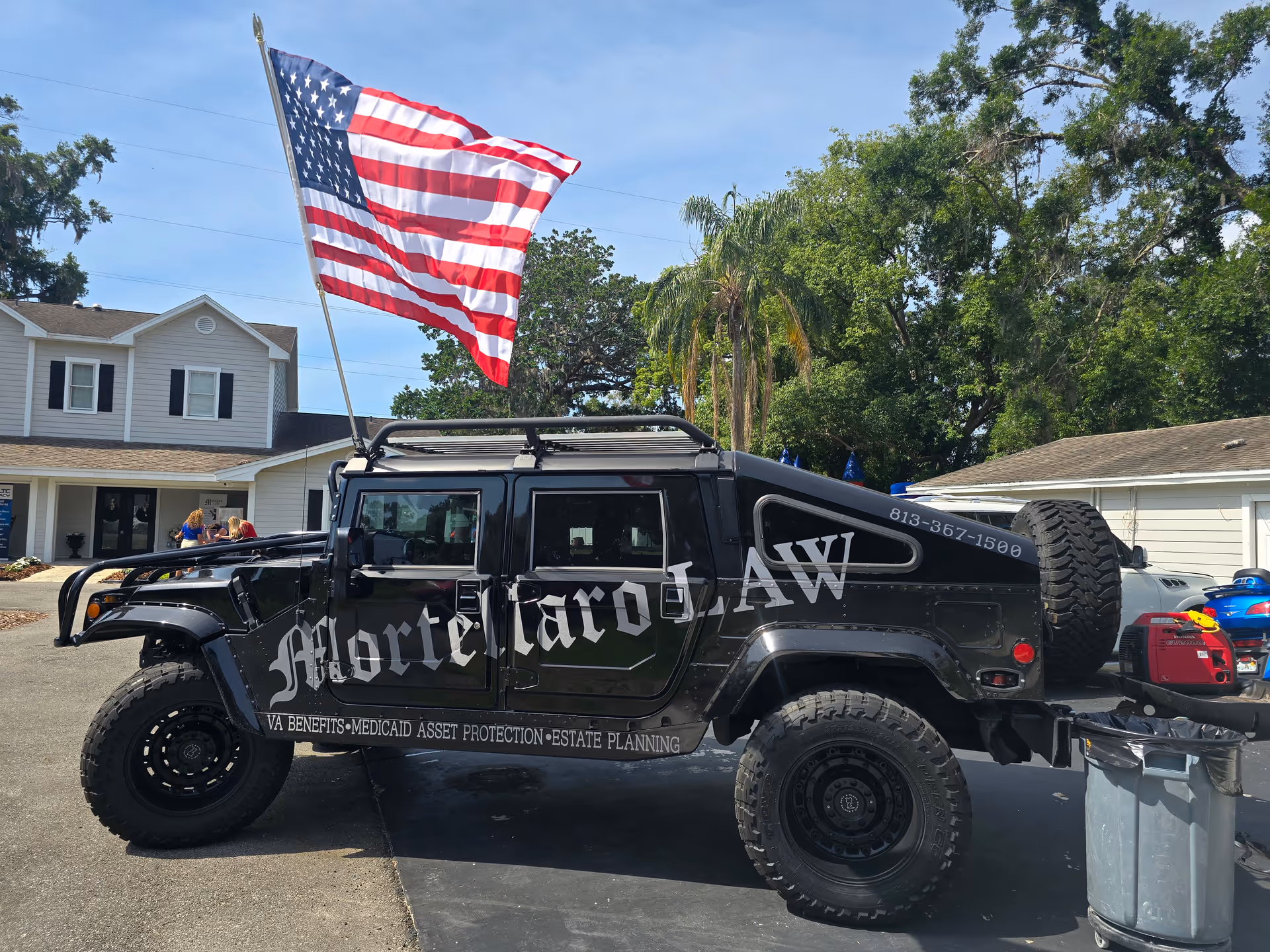A black armored Hummer with an American flag parked outside a residential building