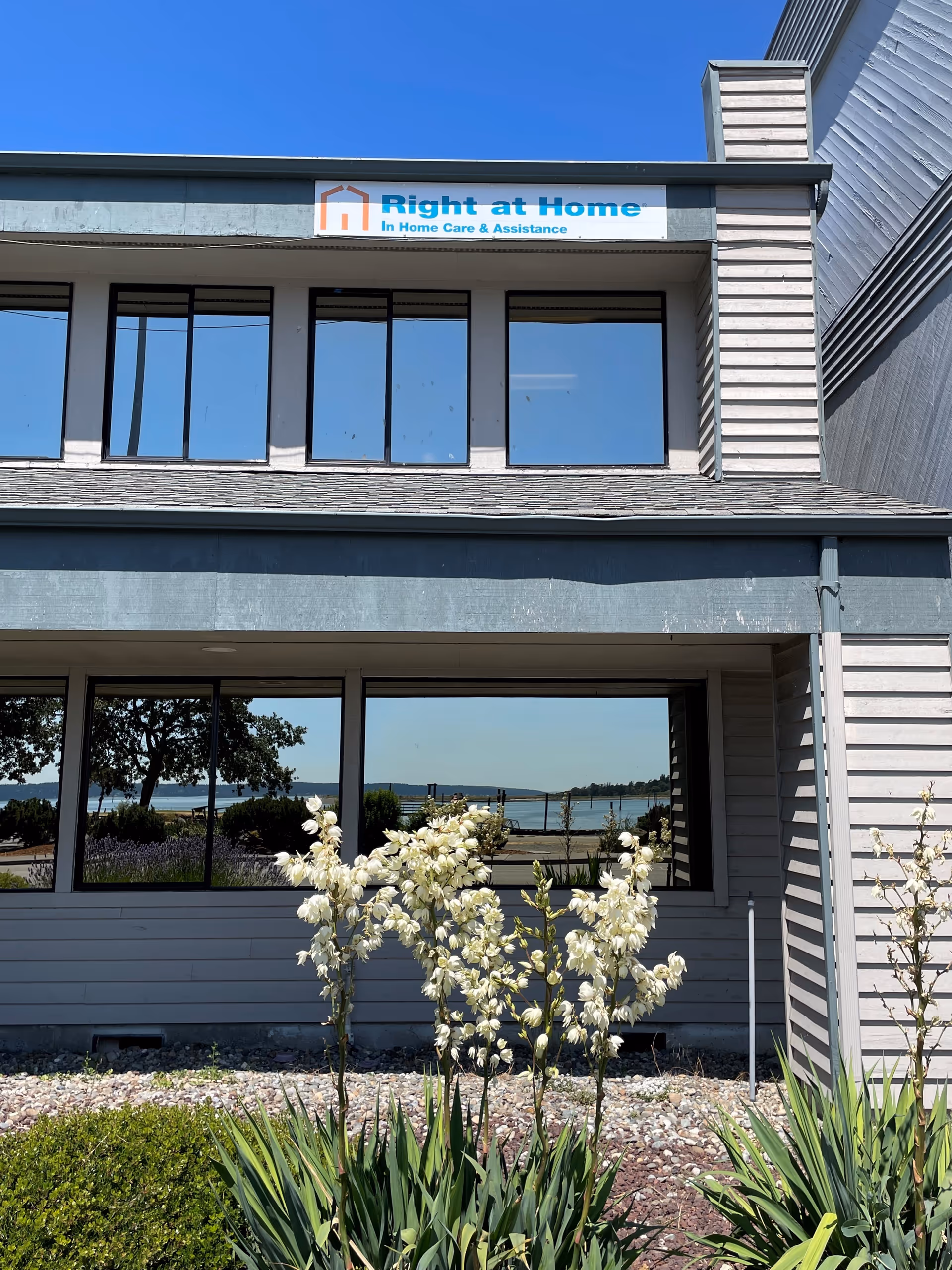 Exterior view of a Right at Home building with signage, windows, and white flowering plants.
