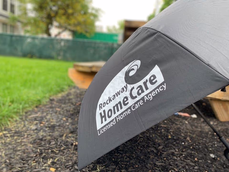 Close up of a large outdoor umbrella with Rockaway Home Care logo in a yard.