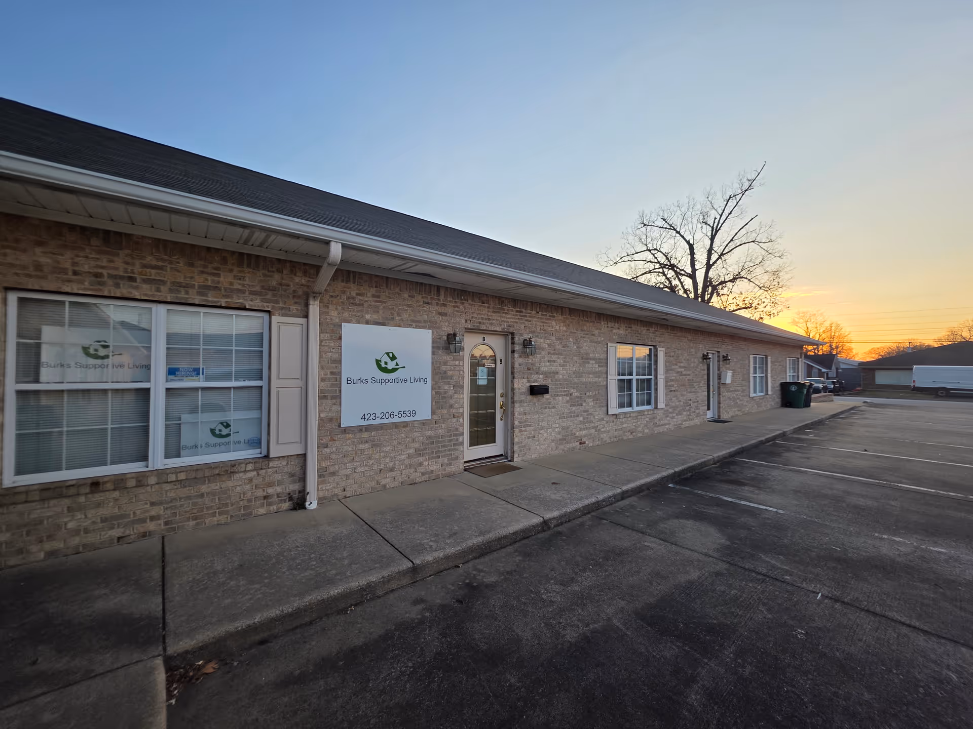 Brick exterior of Burks Supportive Living with entrance and parking lot at sunset.