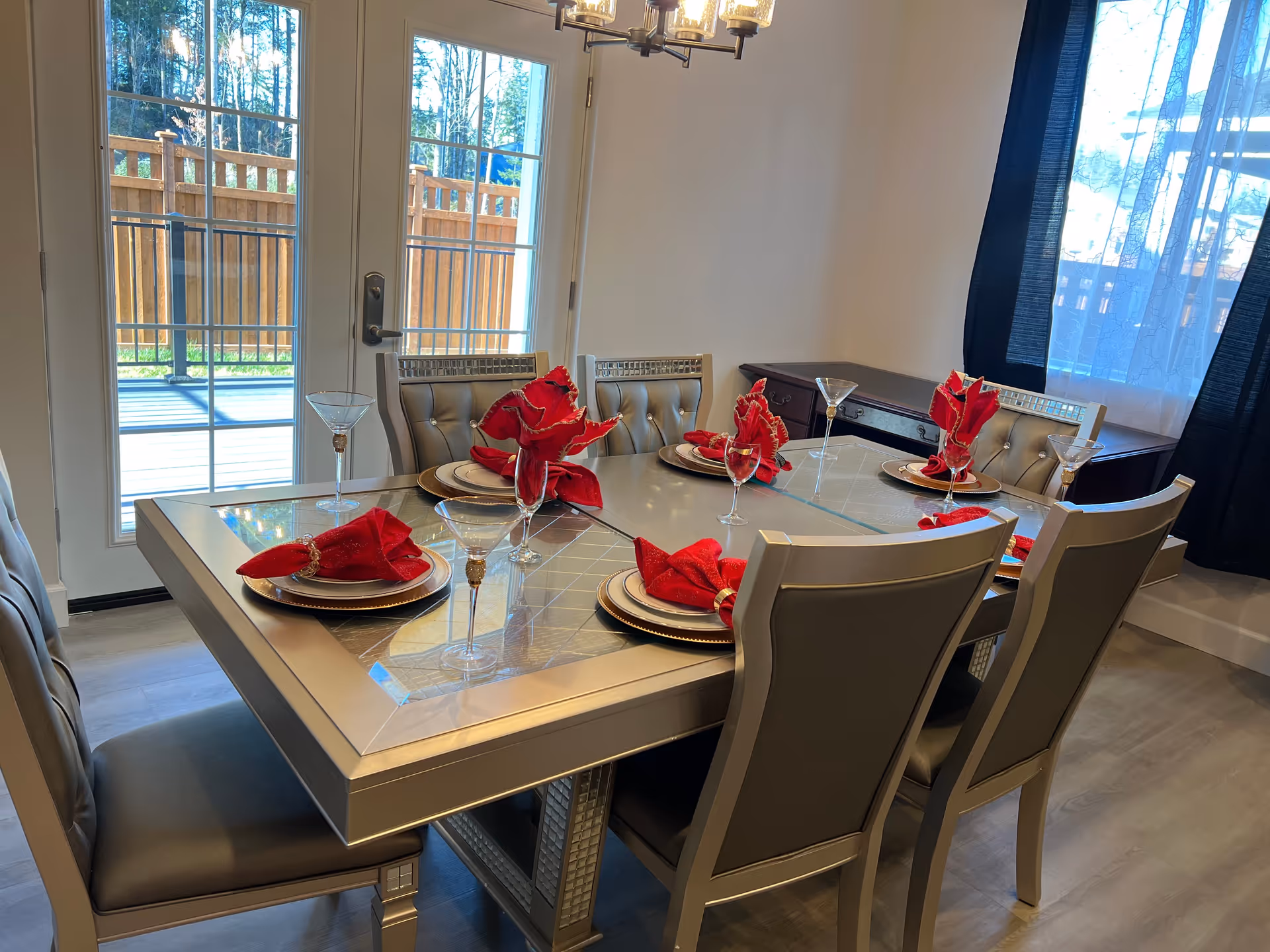 A modern dining room with a glass table set for six and red napkins.