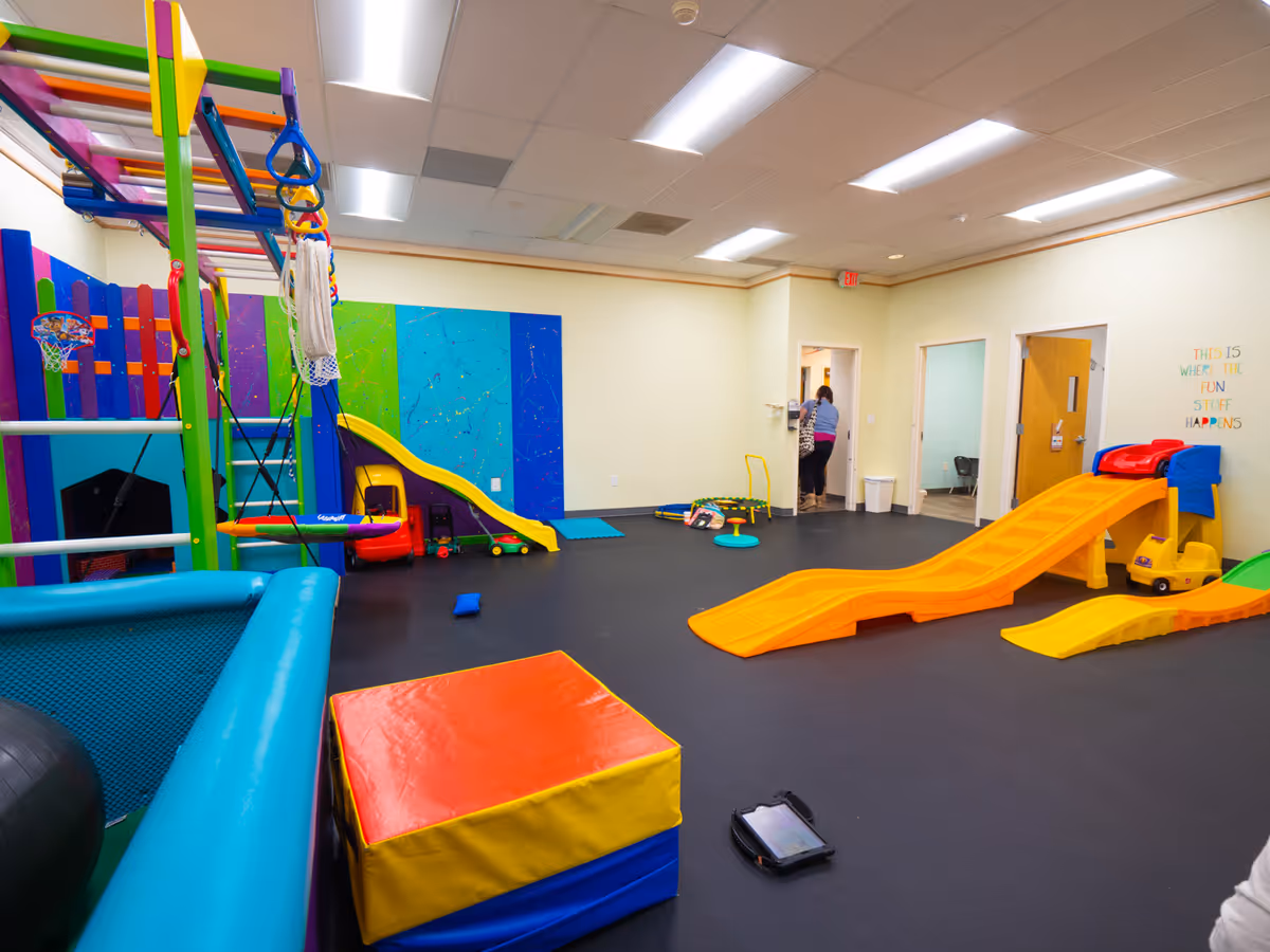 Bright indoor therapy play area with colorful climbing structures, slides, and soft blocks.