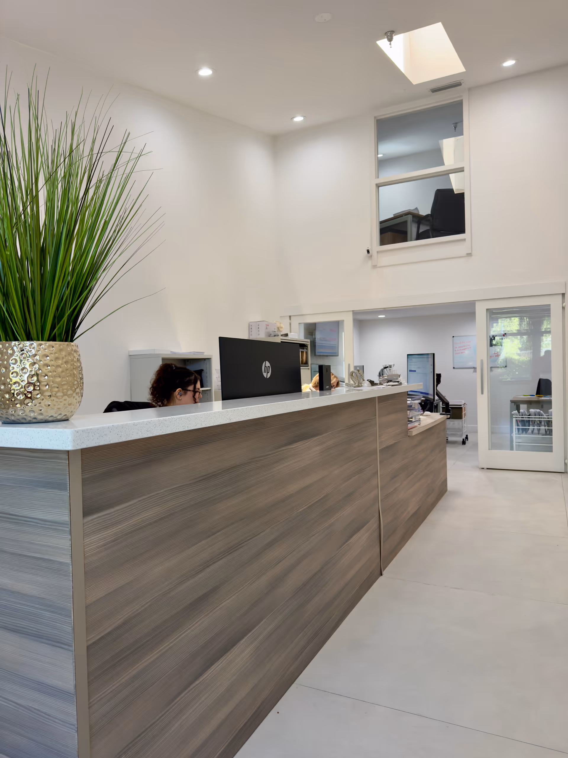 Bright lobby interior with a reception desk, tall plant, computer, and glass doors.