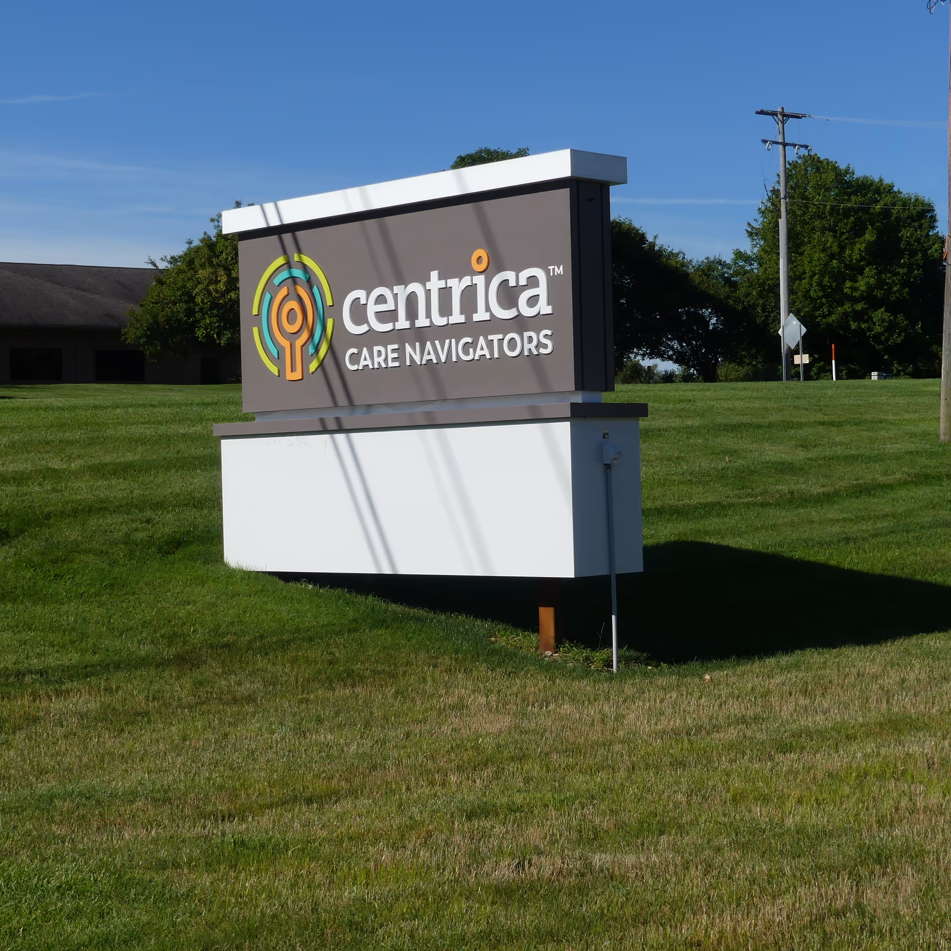 Outdoor grassy area with a Centrica Care Navigators signboard and surrounding trees.