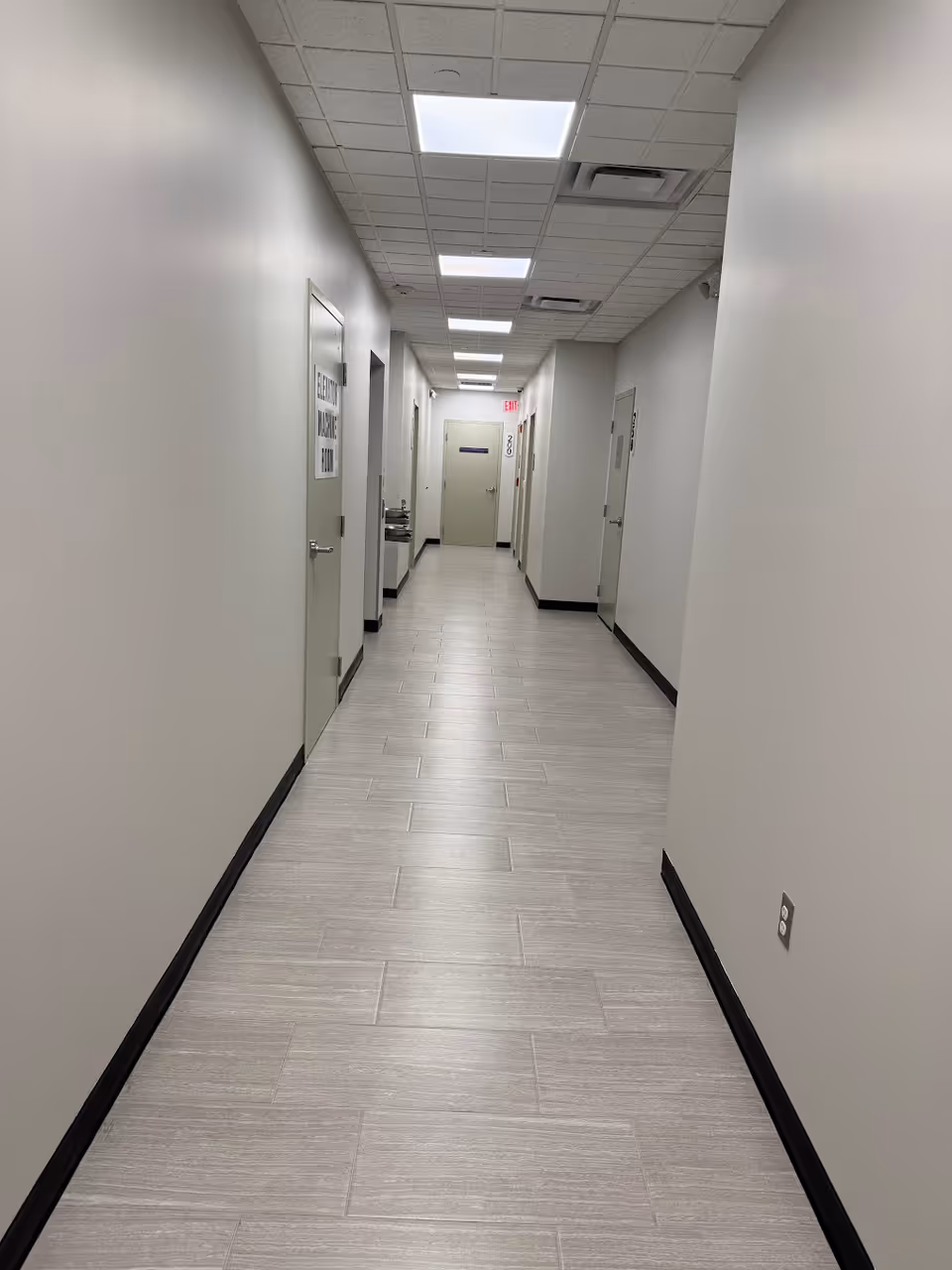 A long, empty hallway with doors on both sides and bright ceiling lights.