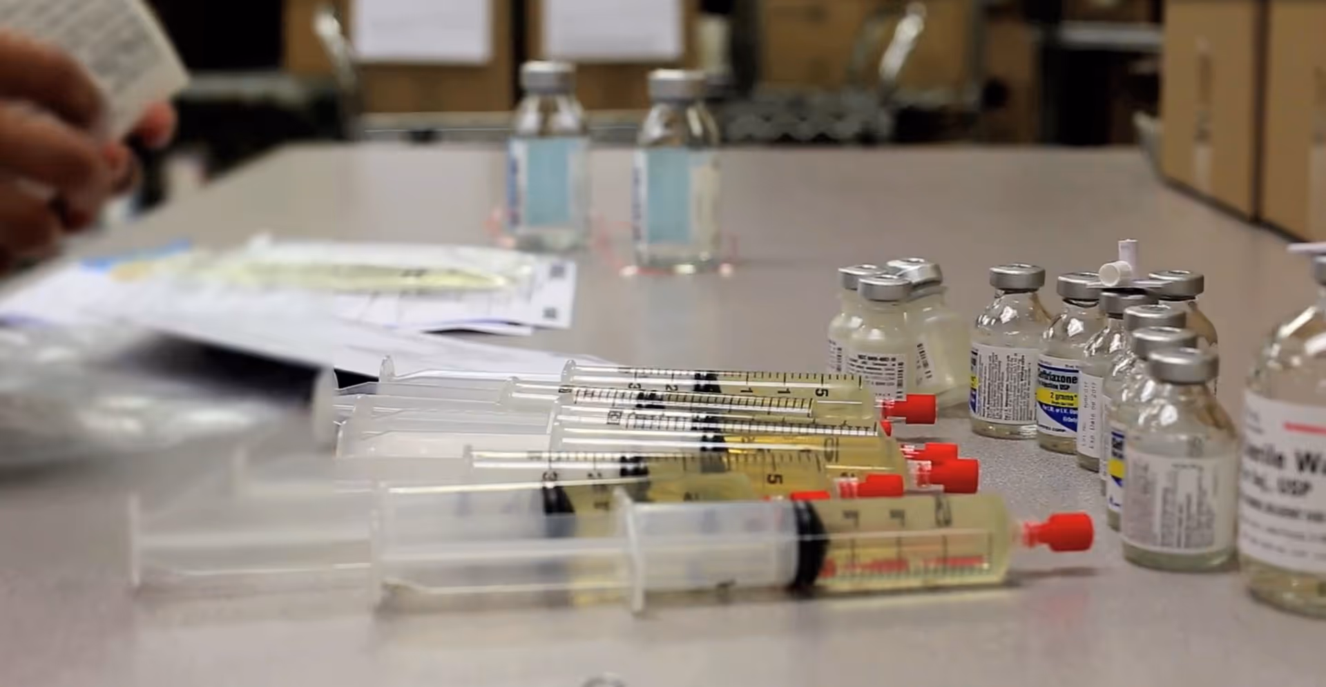 Close-up of syringes and vaccine vials on a table in a facility.
