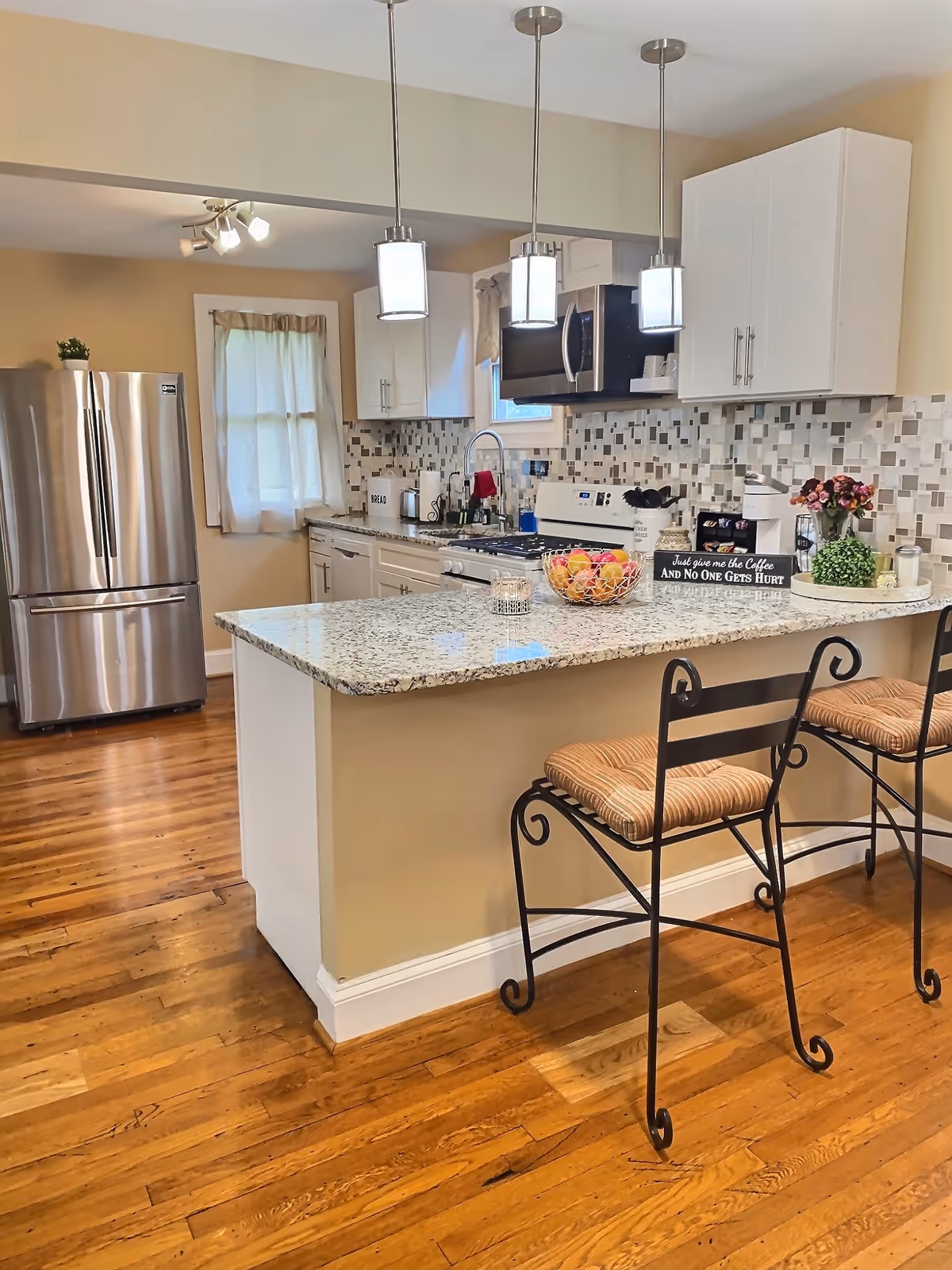 Bright modern kitchen with granite island, pendant lights, stainless steel appliances, and bar stools.