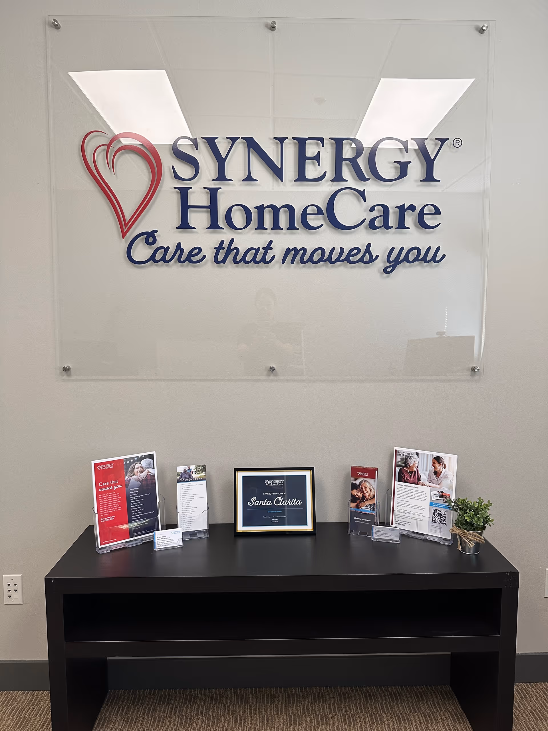 Interior lobby with a SYNERGY HomeCare sign and a black reception desk with pamphlets.