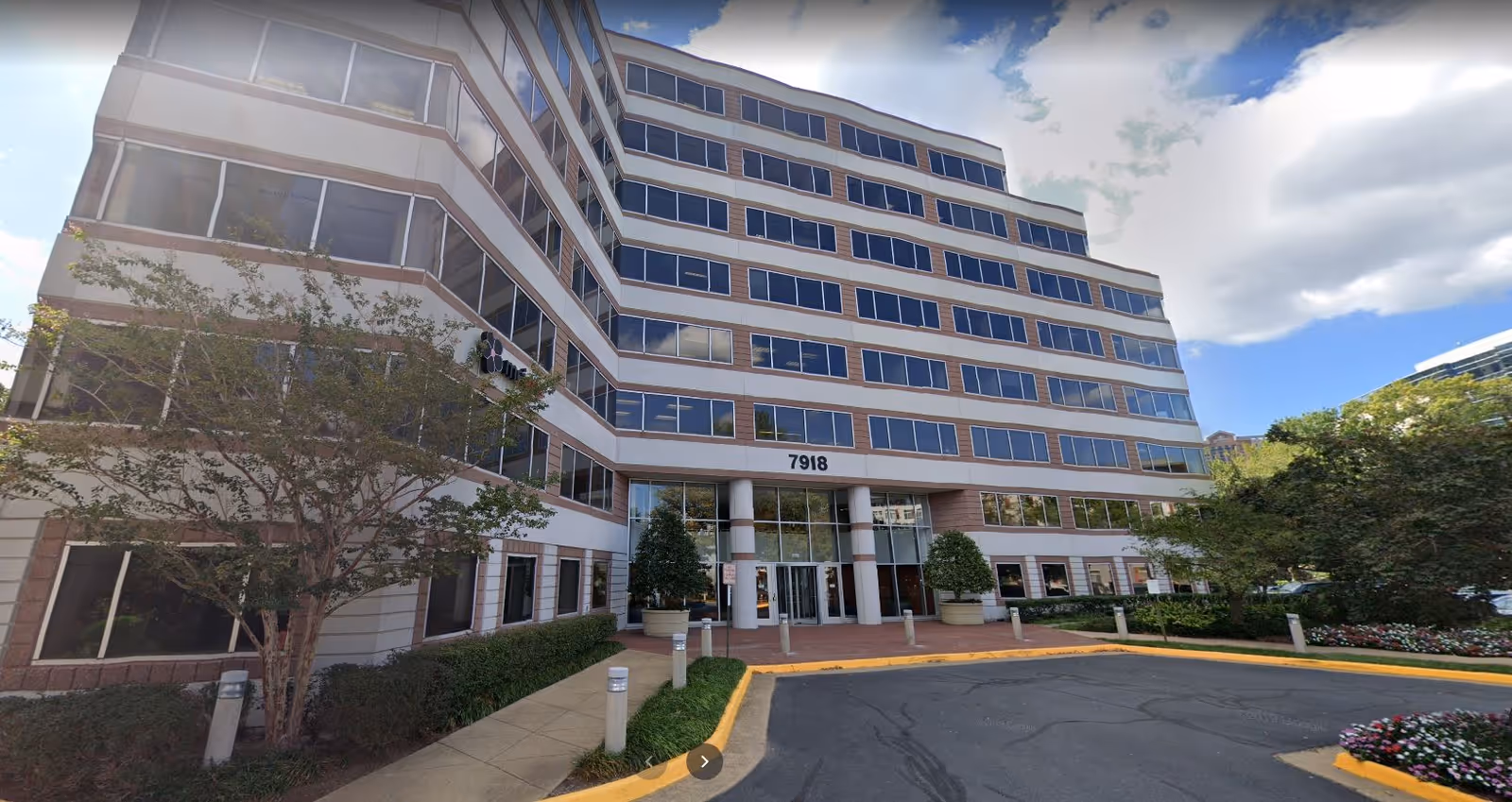 Multi-story senior living building with glass windows, entrance columns, and landscaped driveway.