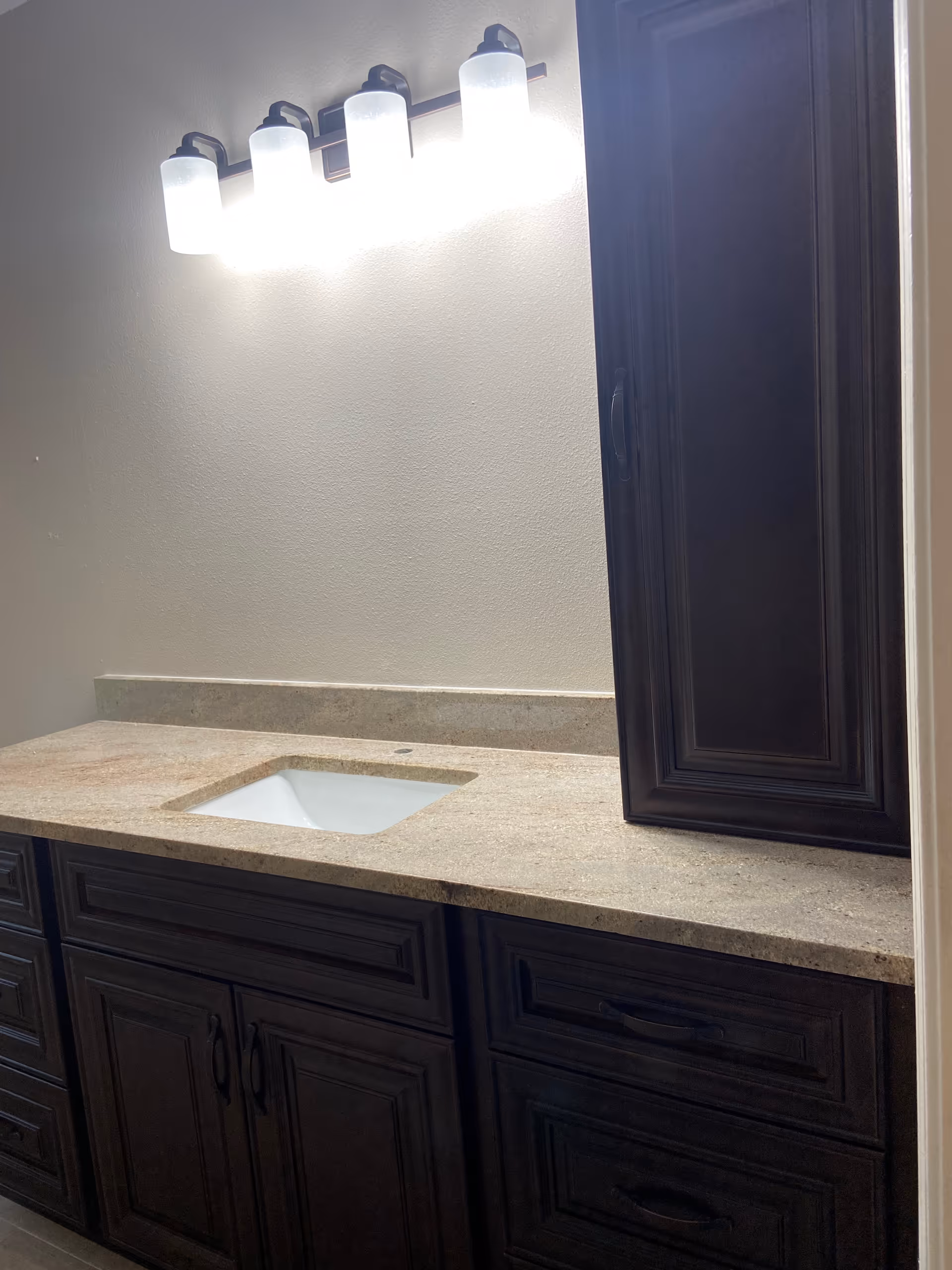 Dark wood bathroom vanity with sink, granite countertop, and bright wall-mounted lights.