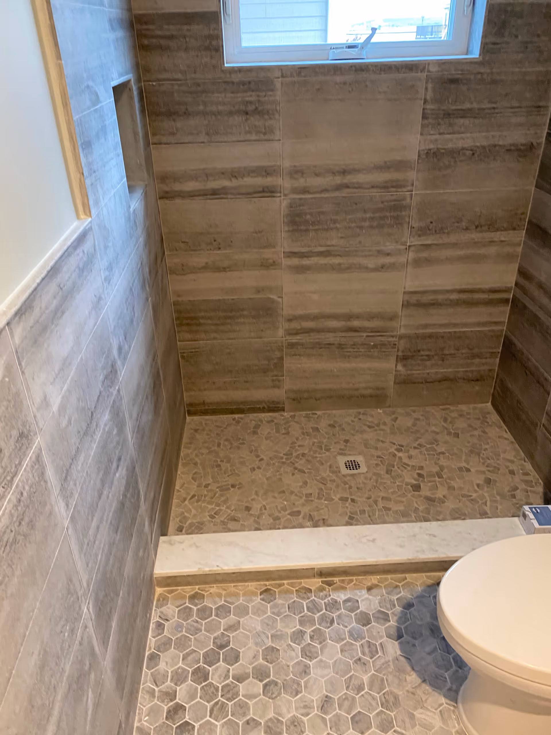 Tiled bathroom with a small window, mosaic floor, and a toilet in the foreground.
