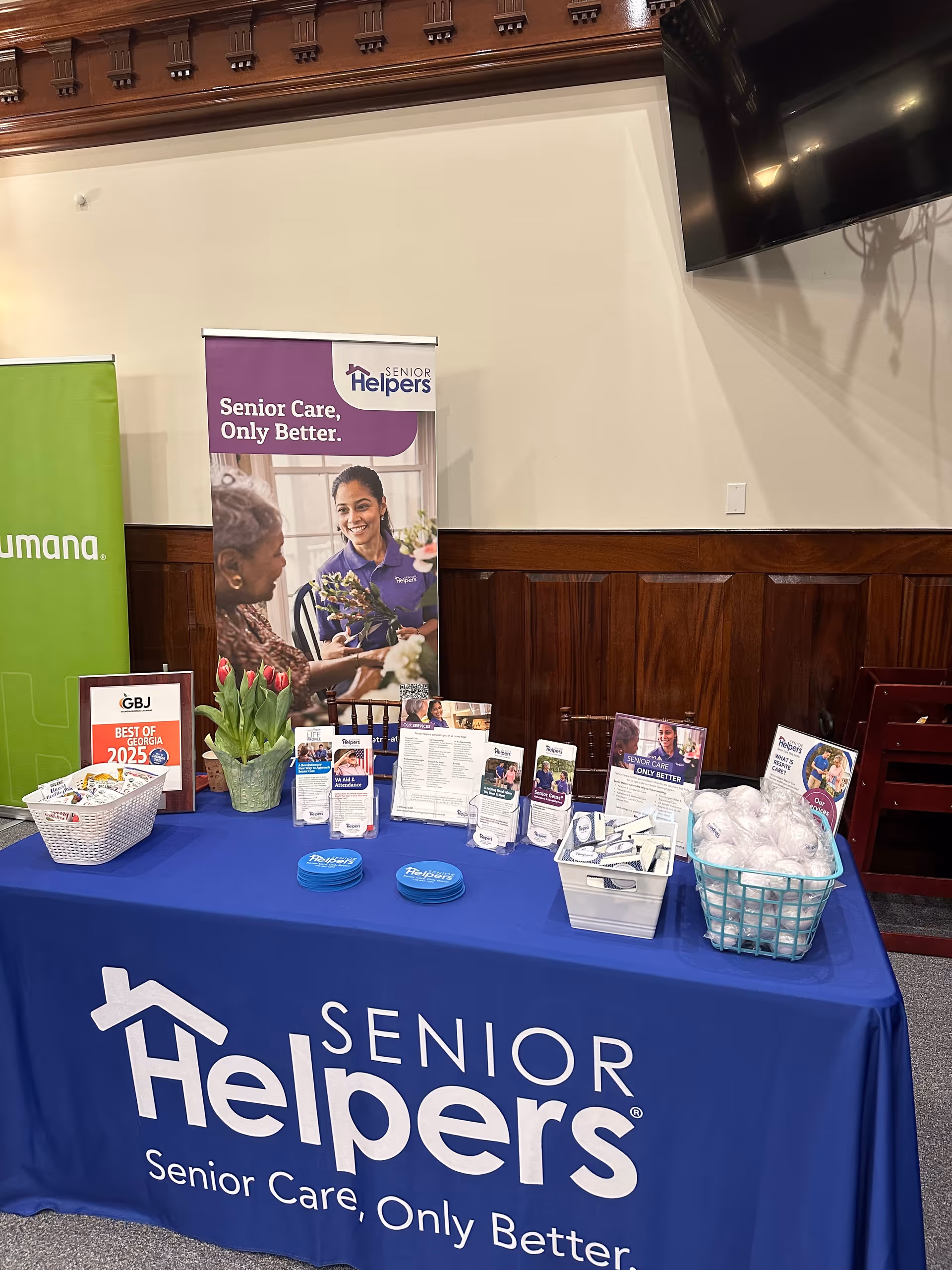 A booth with Senior Helpers banners, brochures, and a blue tablecloth in a hallway.