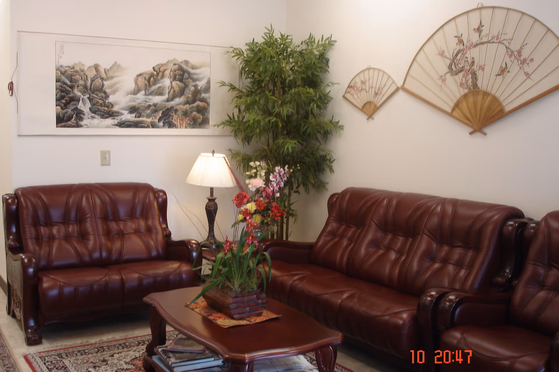 Cozy living room with burgundy leather sofas, wooden coffee table, plants, and wall art.