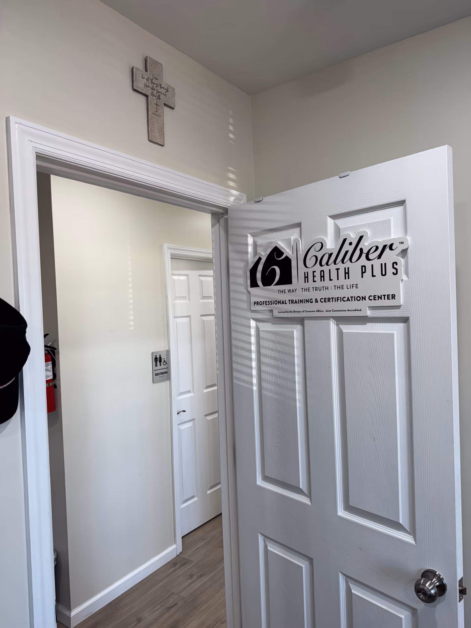 Door displays Caliber Health Plus sign; hallway doorway leads to a training center.