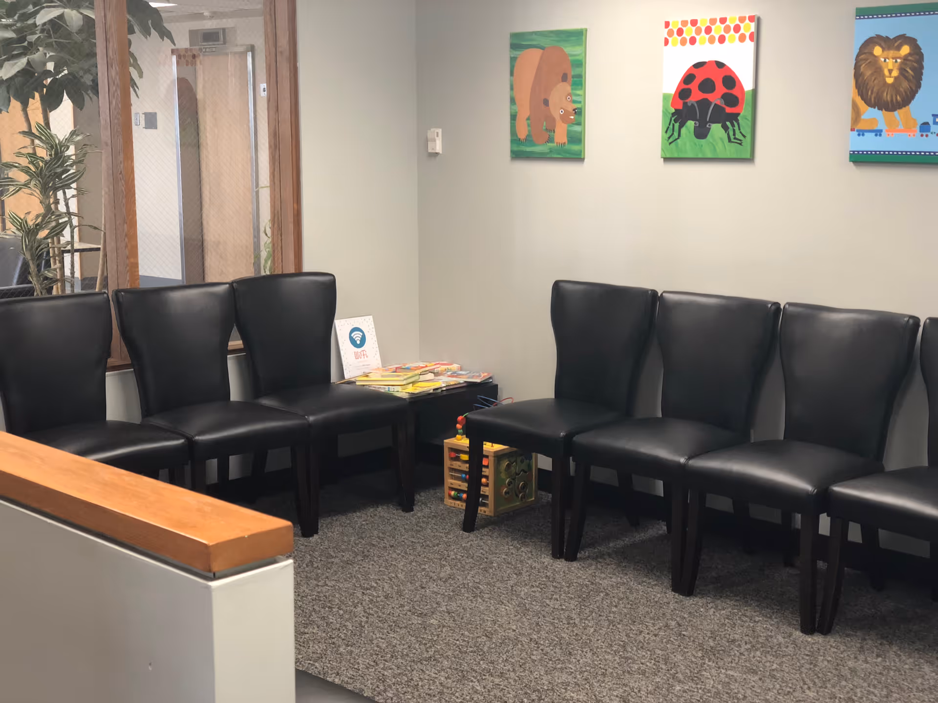 Waiting area with black leather chairs, magazines, and colorful children's artwork.