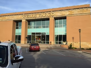 Front view of a Wells Fargo bank with glass entrance, brick facade, and parked cars.