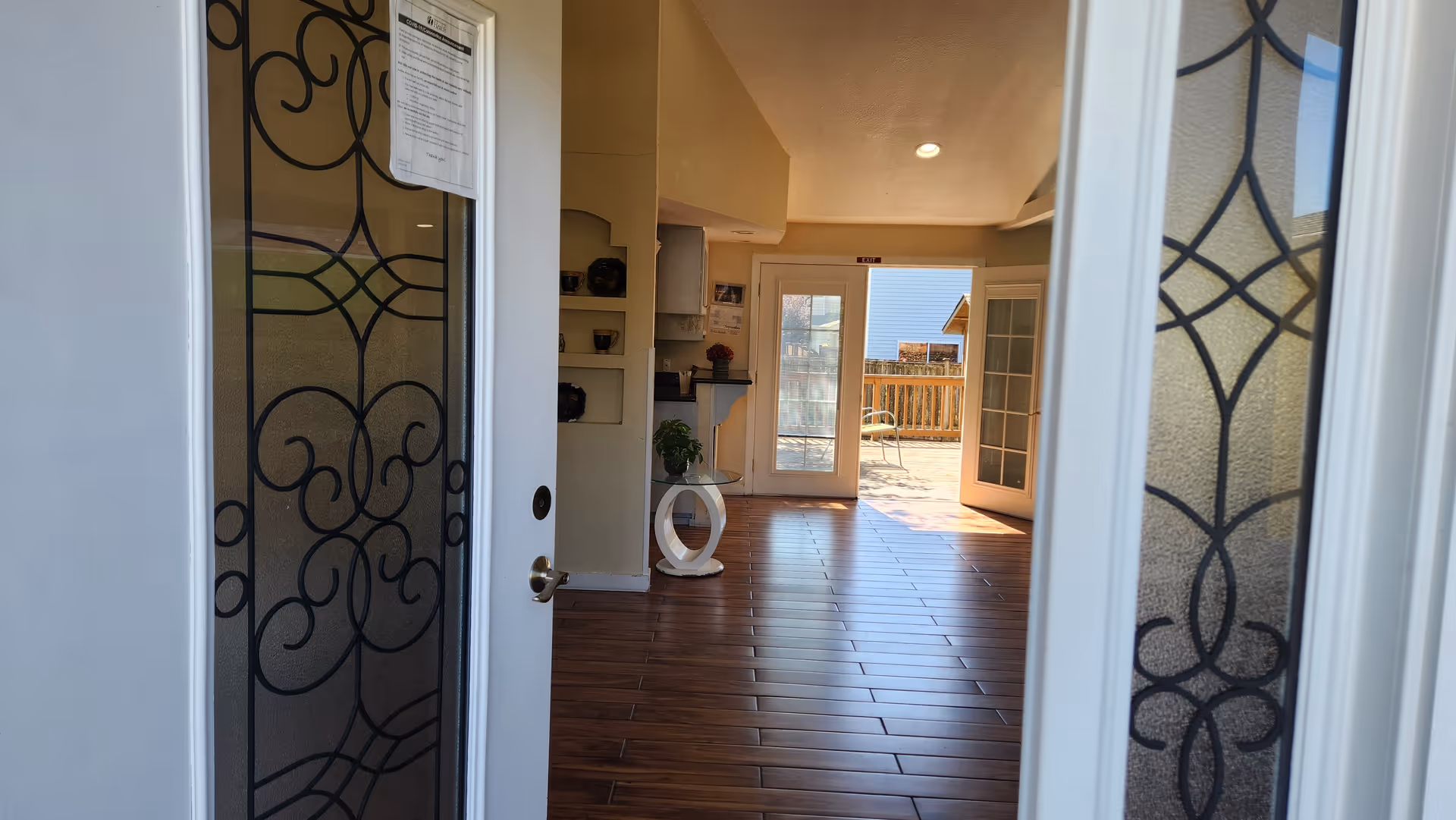 Open doorway reveals a bright interior with wooden floor tiles and an outdoor deck beyond.