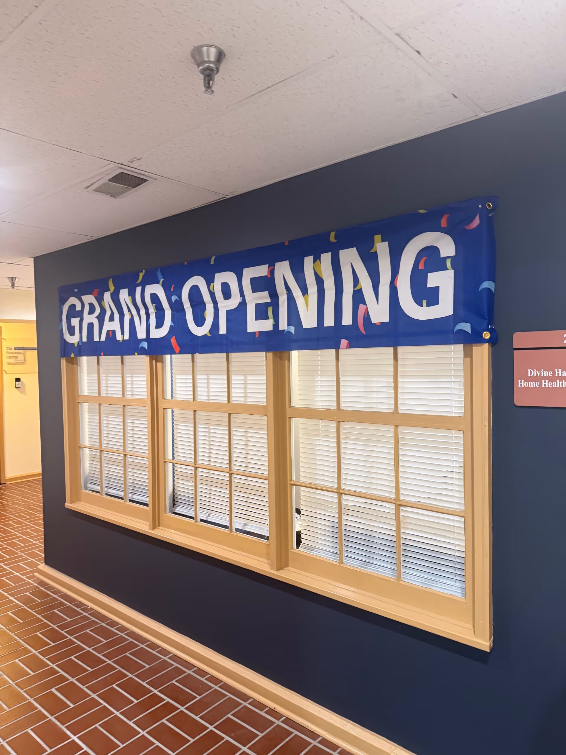 Blue interior hallway with a large Grand Opening banner above a windowed wall.