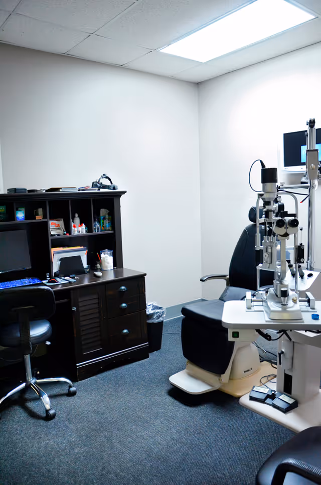 Eye clinic exam room with slit lamp, exam chair, computer desk, and shelves.