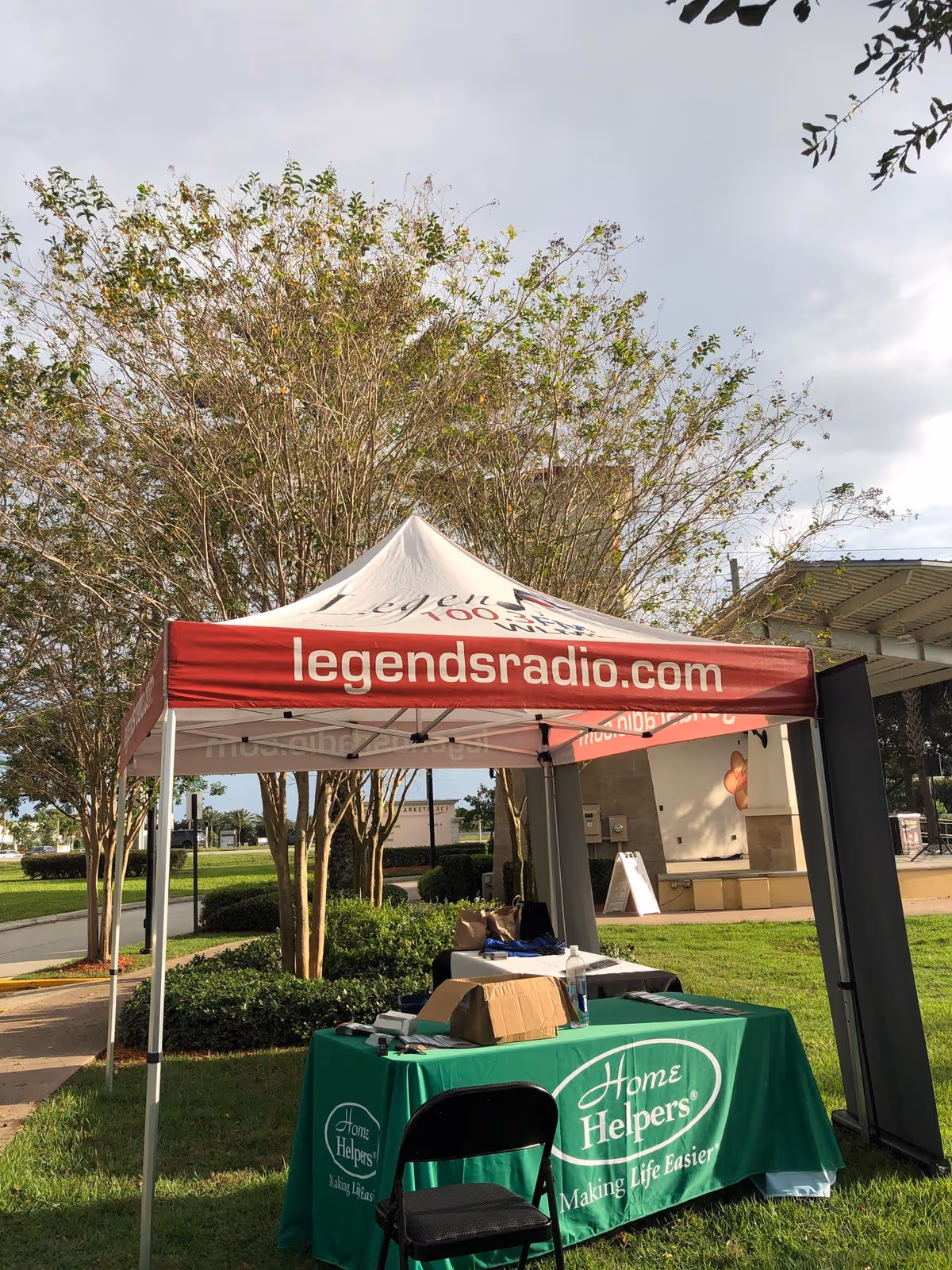 Outdoor event tent with Home Helpers table and signage in a park-like setting.
