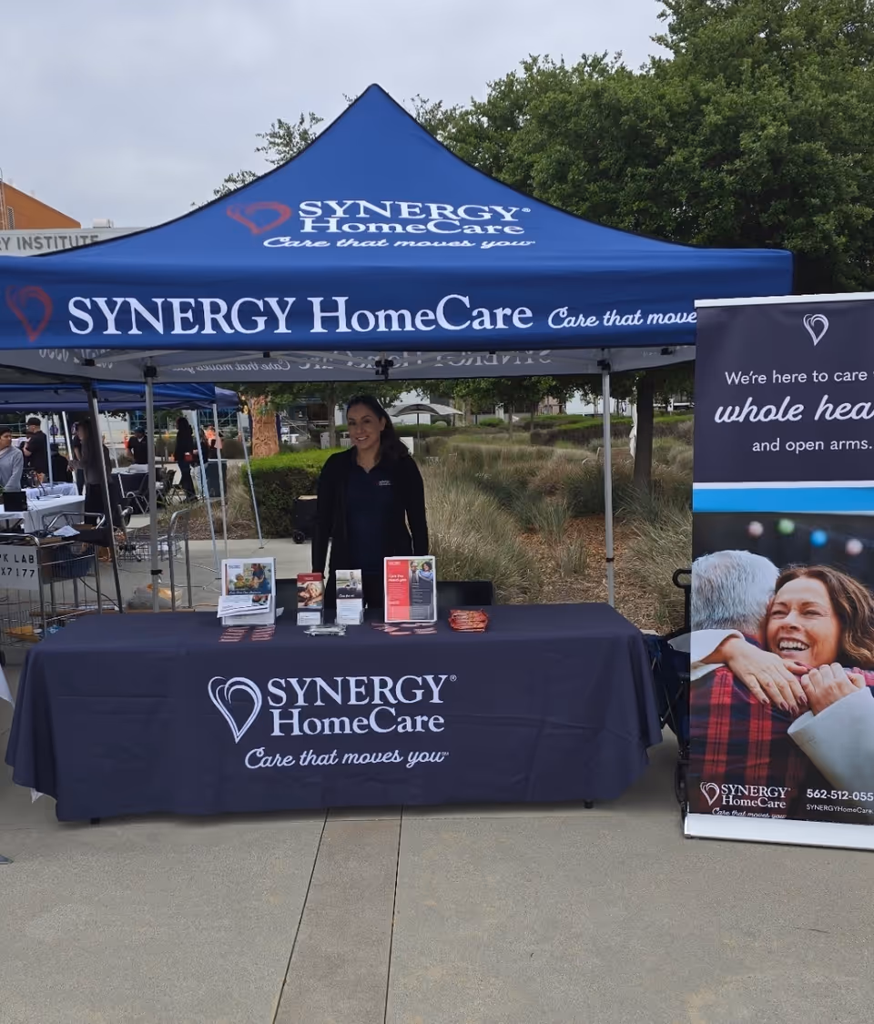 Outdoor Synergy HomeCare booth with a smiling staff member and promotional materials