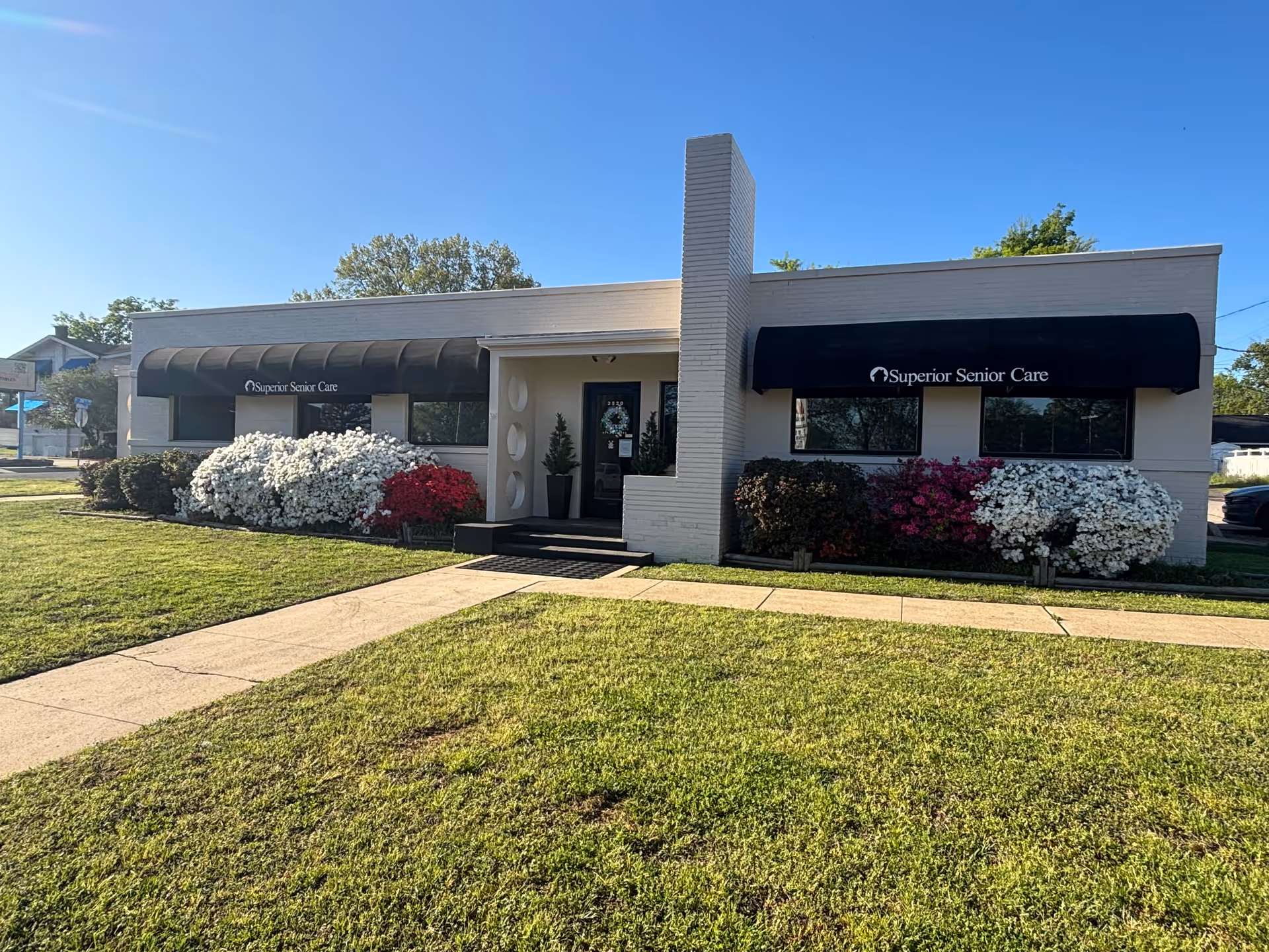 Front view of a single-story senior care facility with awnings and blooming shrubs.