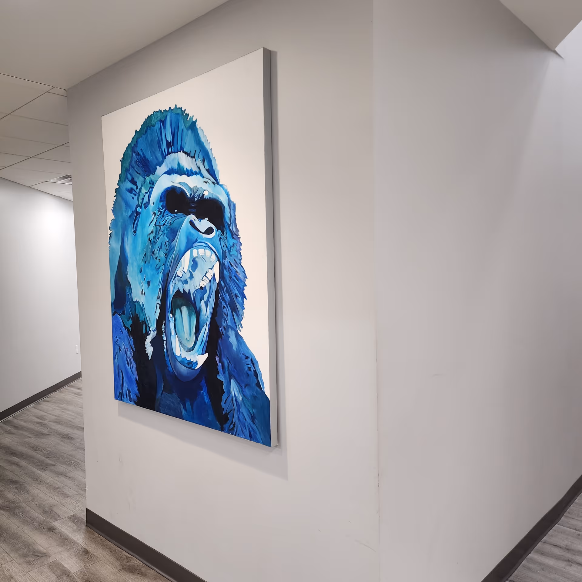 A blue gorilla artwork hangs on a white hallway wall in a modern facility.