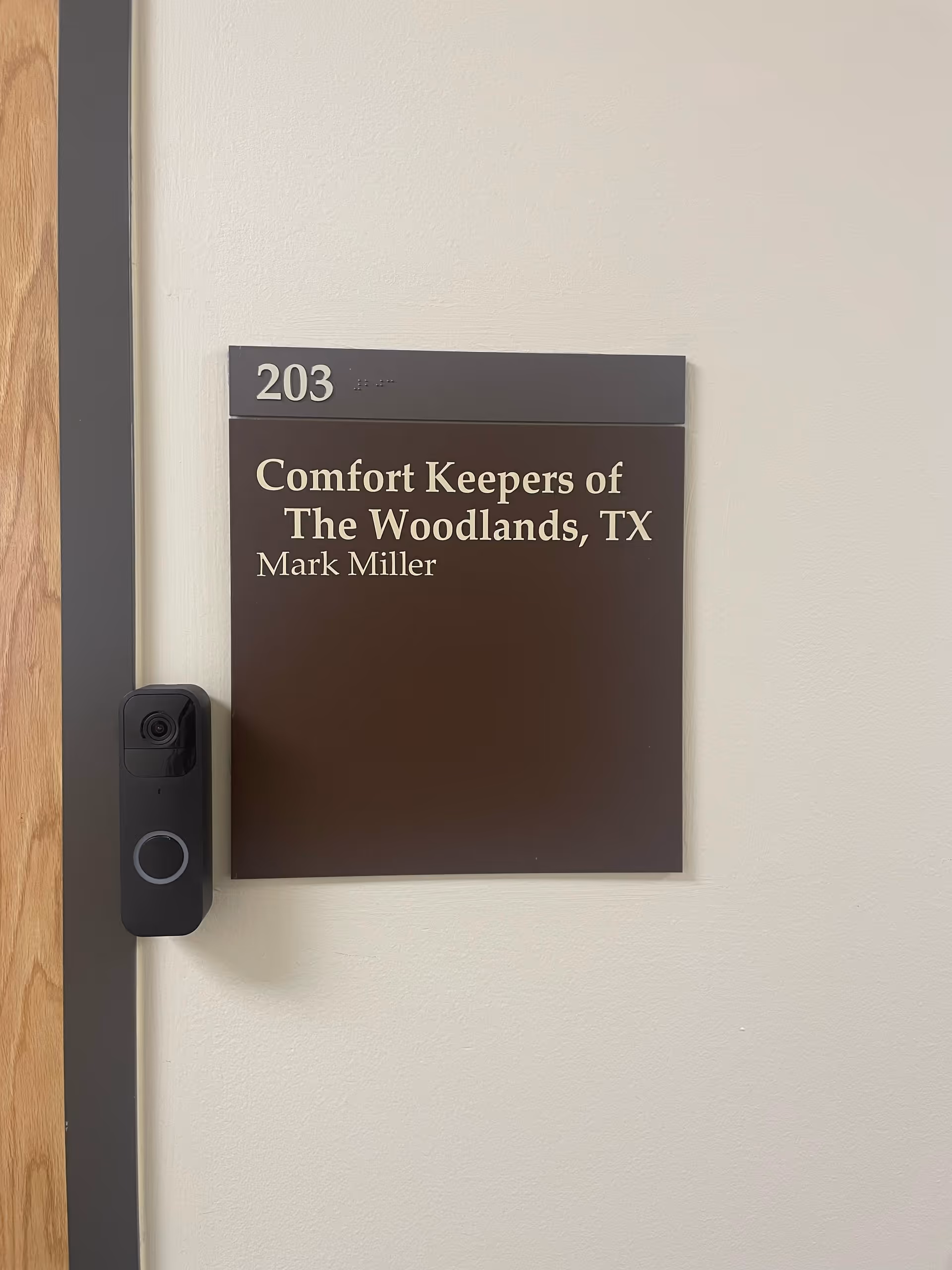 Interior wall with door plaque reading Comfort Keepers of The Woodlands, TX, room 203.