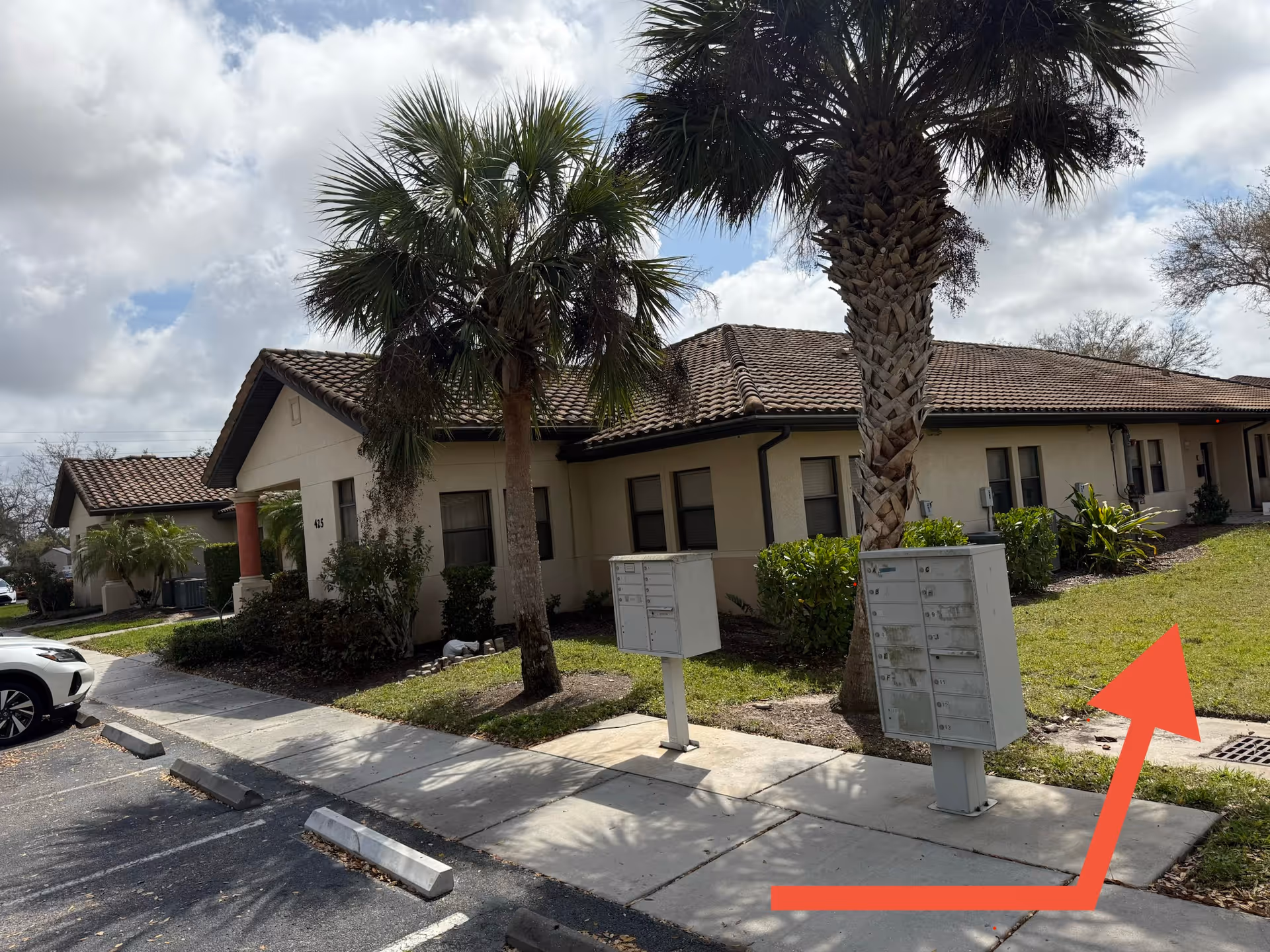 Single-story beige senior living building with palm trees, mailboxes, and a parking lot