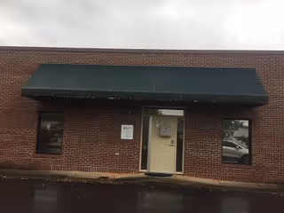 Brick facility exterior with a green awning over a white entrance door.