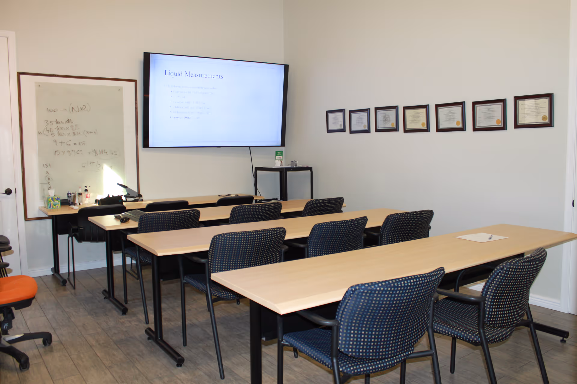 Training room with whiteboard, projector screen, framed certificates, and long communal desks.